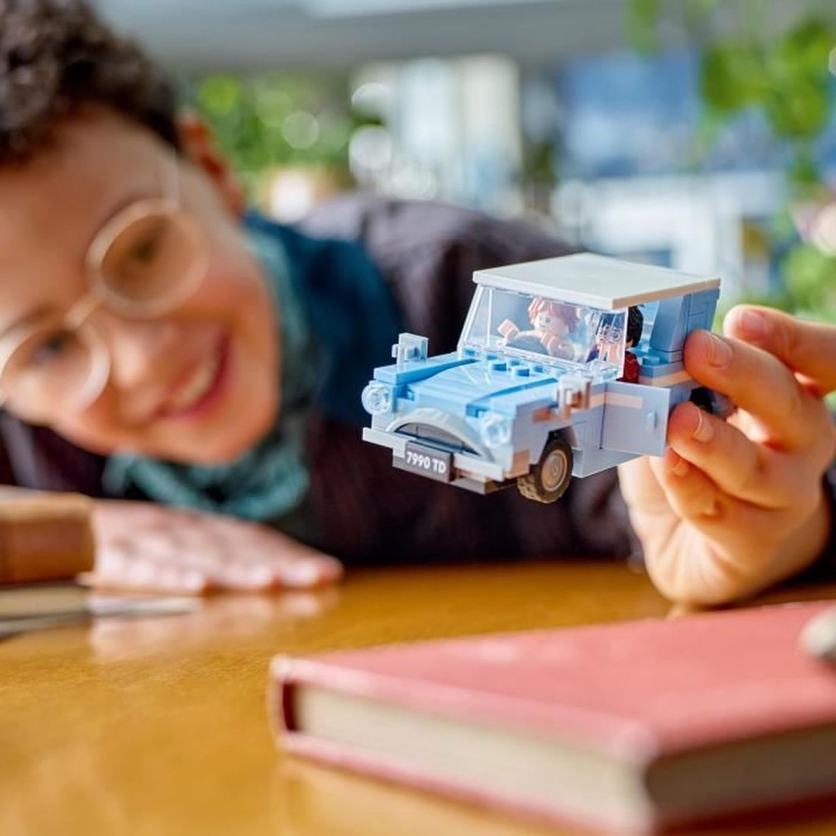 Ein Junge mit Brille spielt mit einem blauen Lego-Auto, in dem Figuren sitzen.