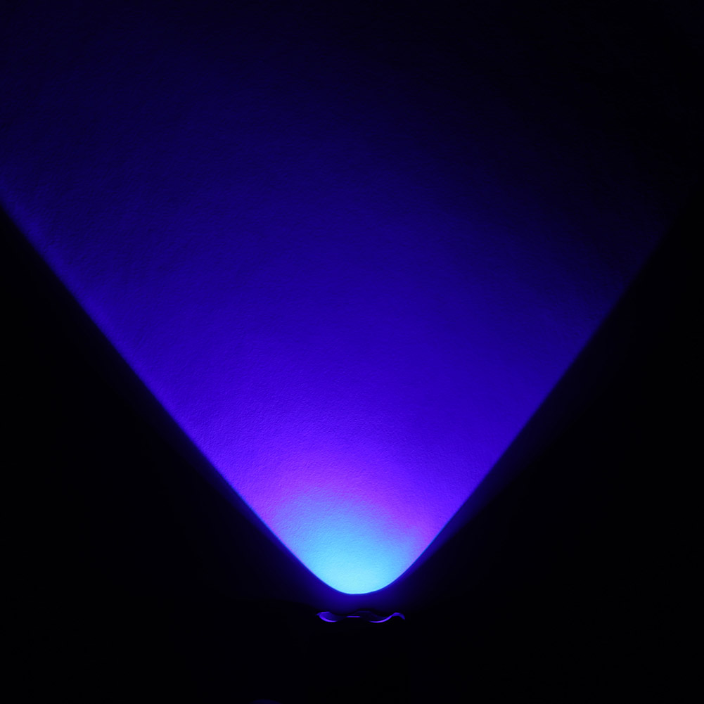 Ein blauer Lichtkegel beleuchtet eine Wand von unten. Der Lichtkegel ist unten hellblau und oben violett.