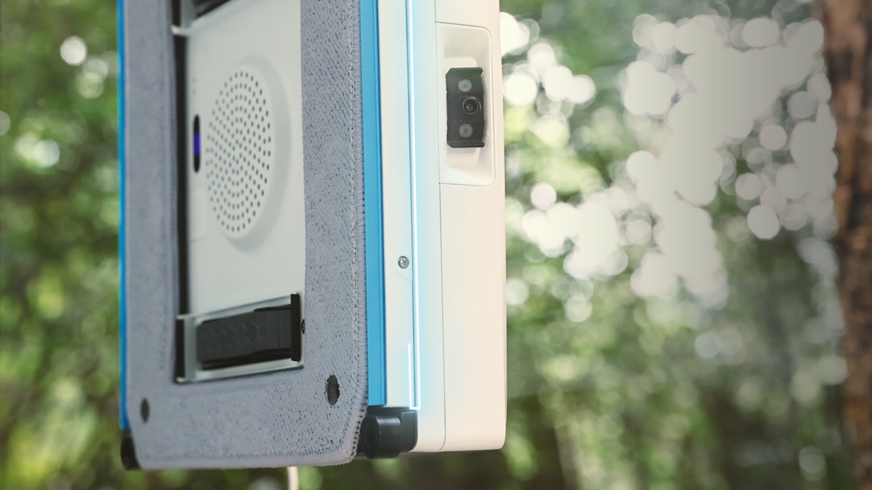 Un robot limpiacristales blanco con detalles azules se adhiere a una ventana.