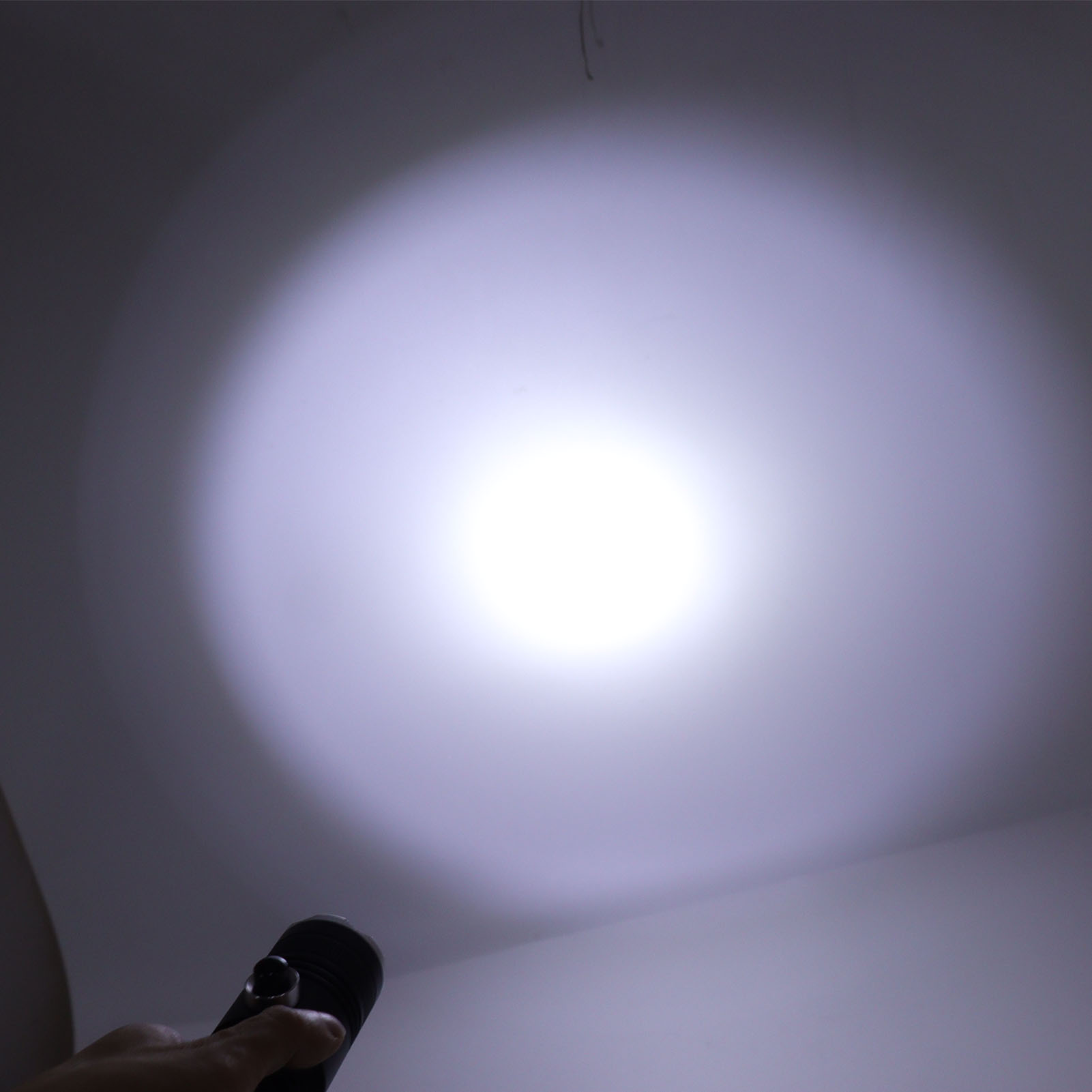 Eine Hand hält eine schwarze Taschenlampe, die einen hellen Lichtstrahl wirft.