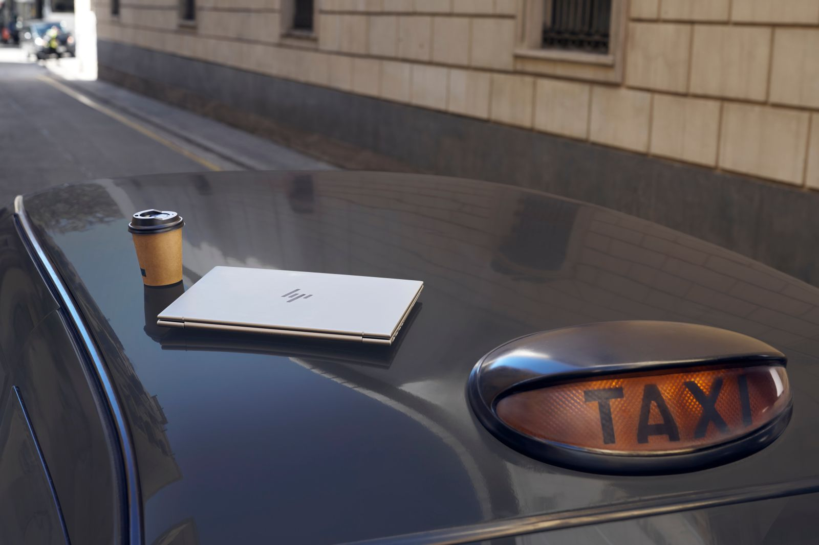 Srebrny laptop i kubek z kawą na czarnym dachu samochodu z tablicą taxi.