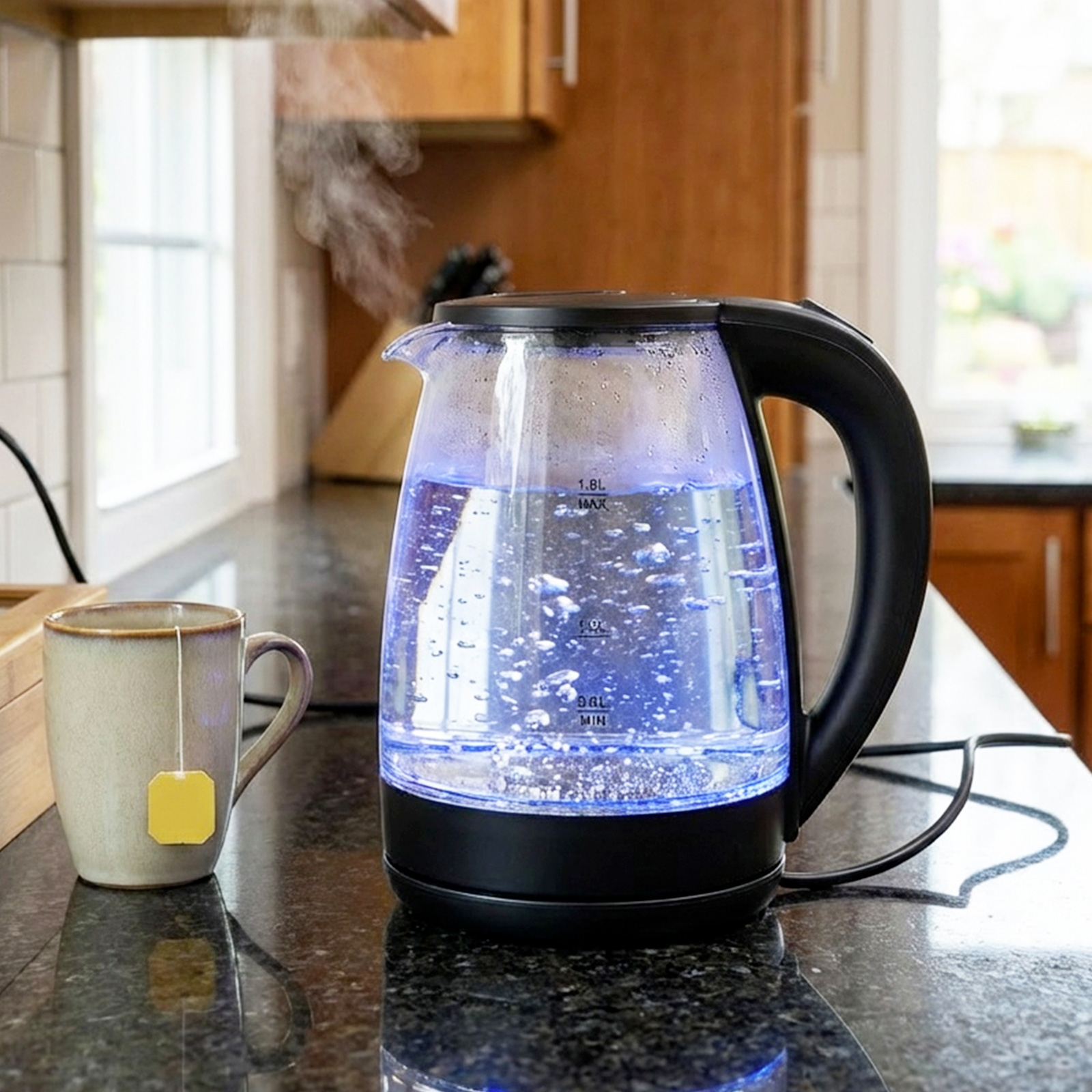 Une bouilloire électrique transparente à lumière bleue fait bouillir de l'eau. Une tasse avec un sachet de thé est à côté.