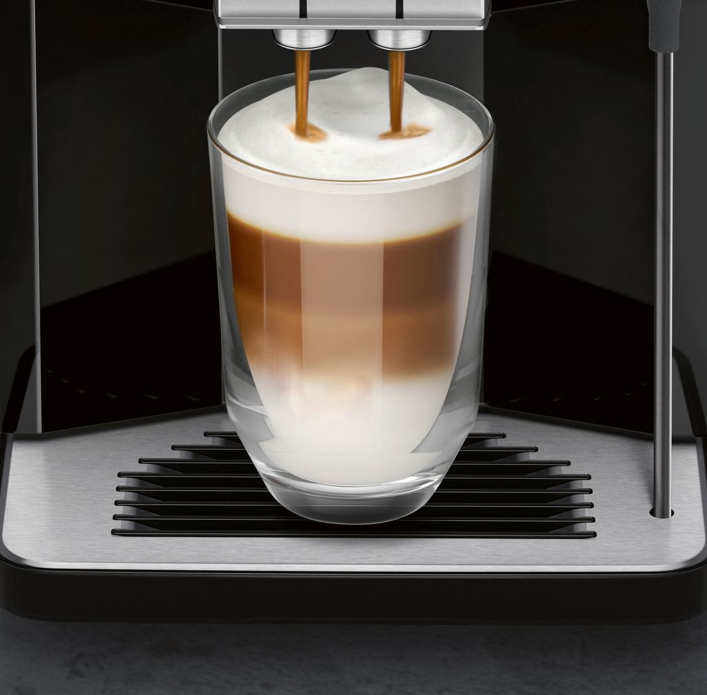 Du café coule dans un verre avec lait et mousse, couches visibles.