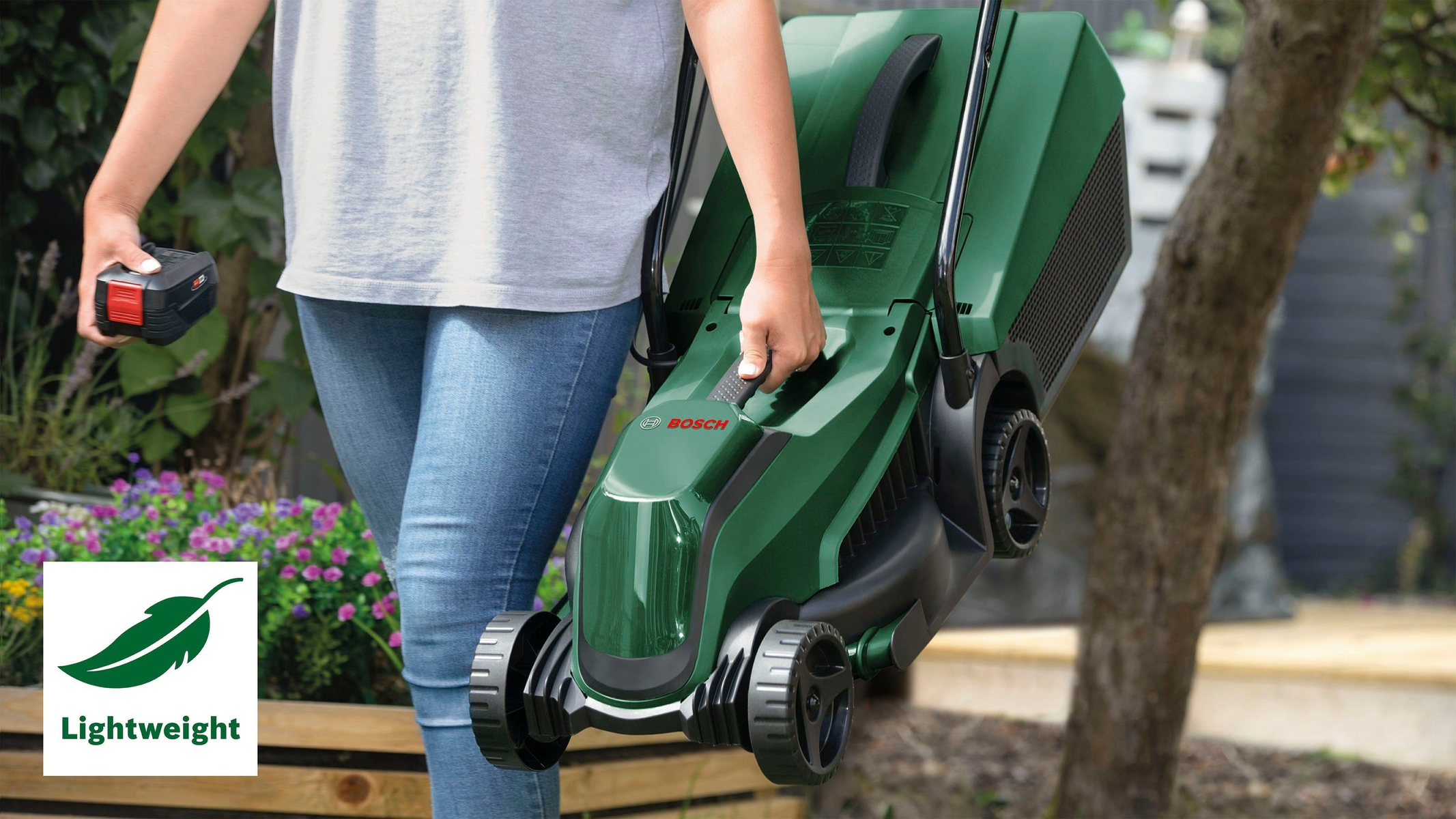 Person trägt einen grünen Bosch Rasenmäher mit Akku im Garten.