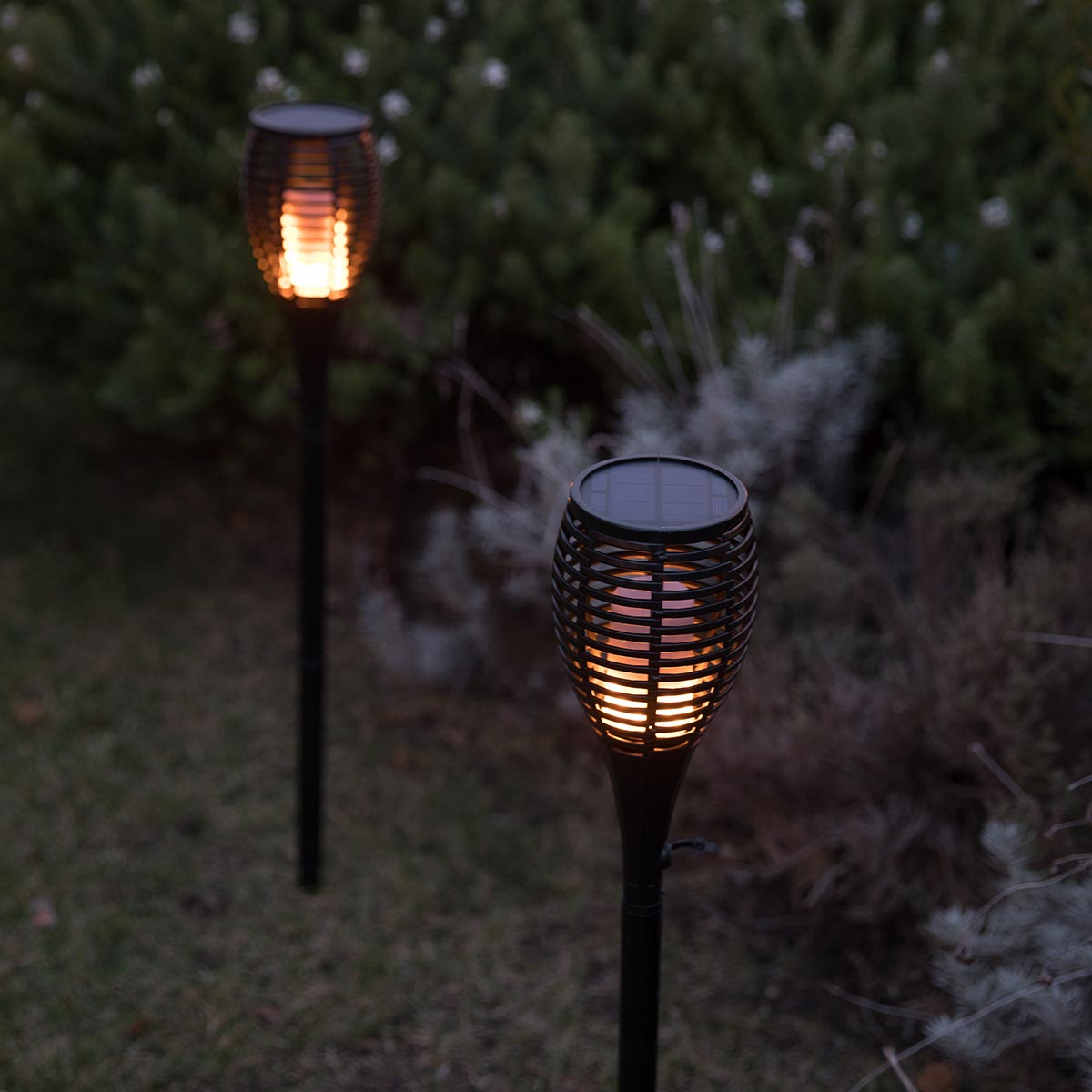 Zwei Solarleuchten mit Flammeneffekt leuchten im Garten bei Nacht.