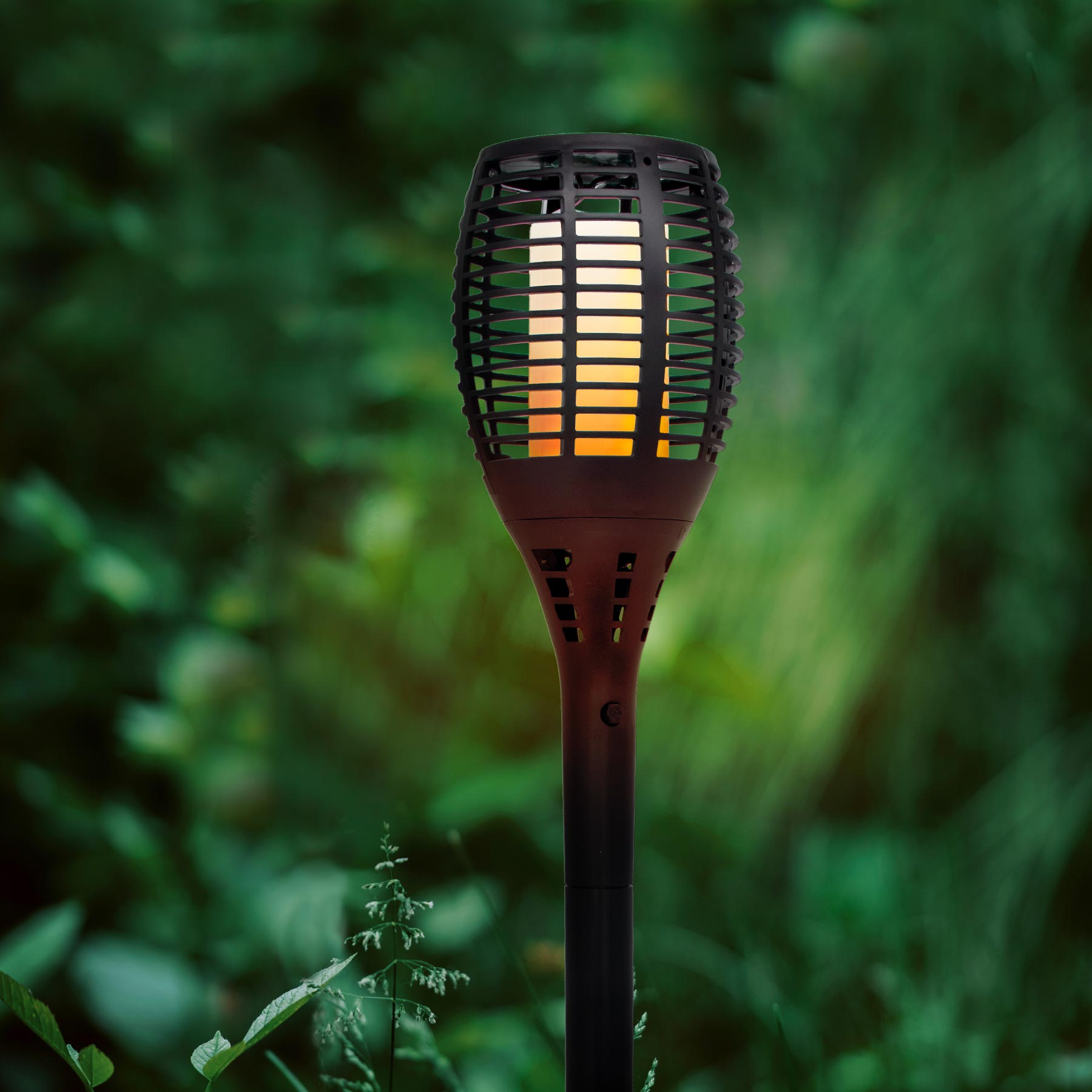 Eine Solar-Gartenfackel mit Flammeneffekt steht im Gras.