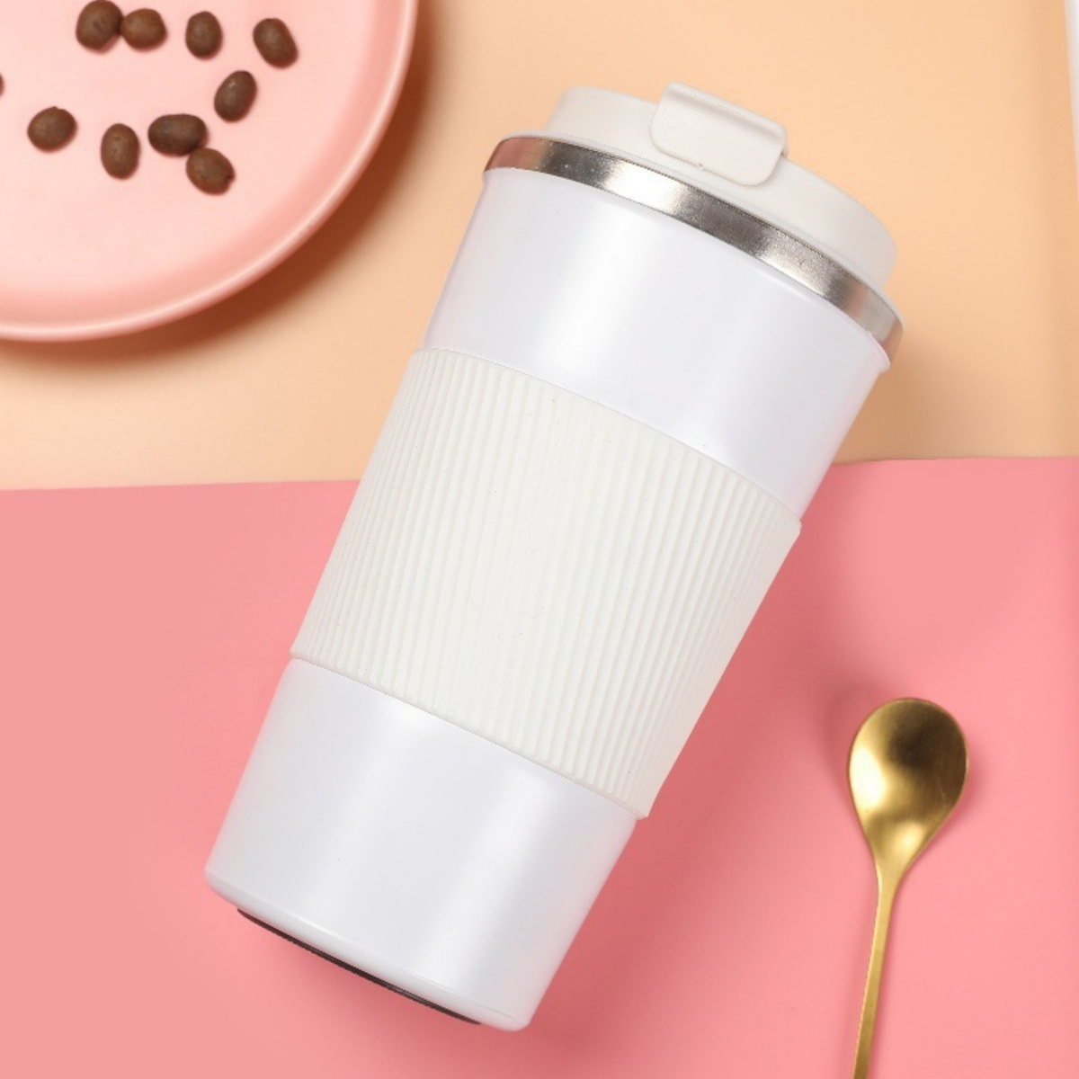 Eine weiße Thermoskanne mit weißem Gummigriff, daneben eine rosa Platte mit Kaffeebohnen und ein goldener Löffel.