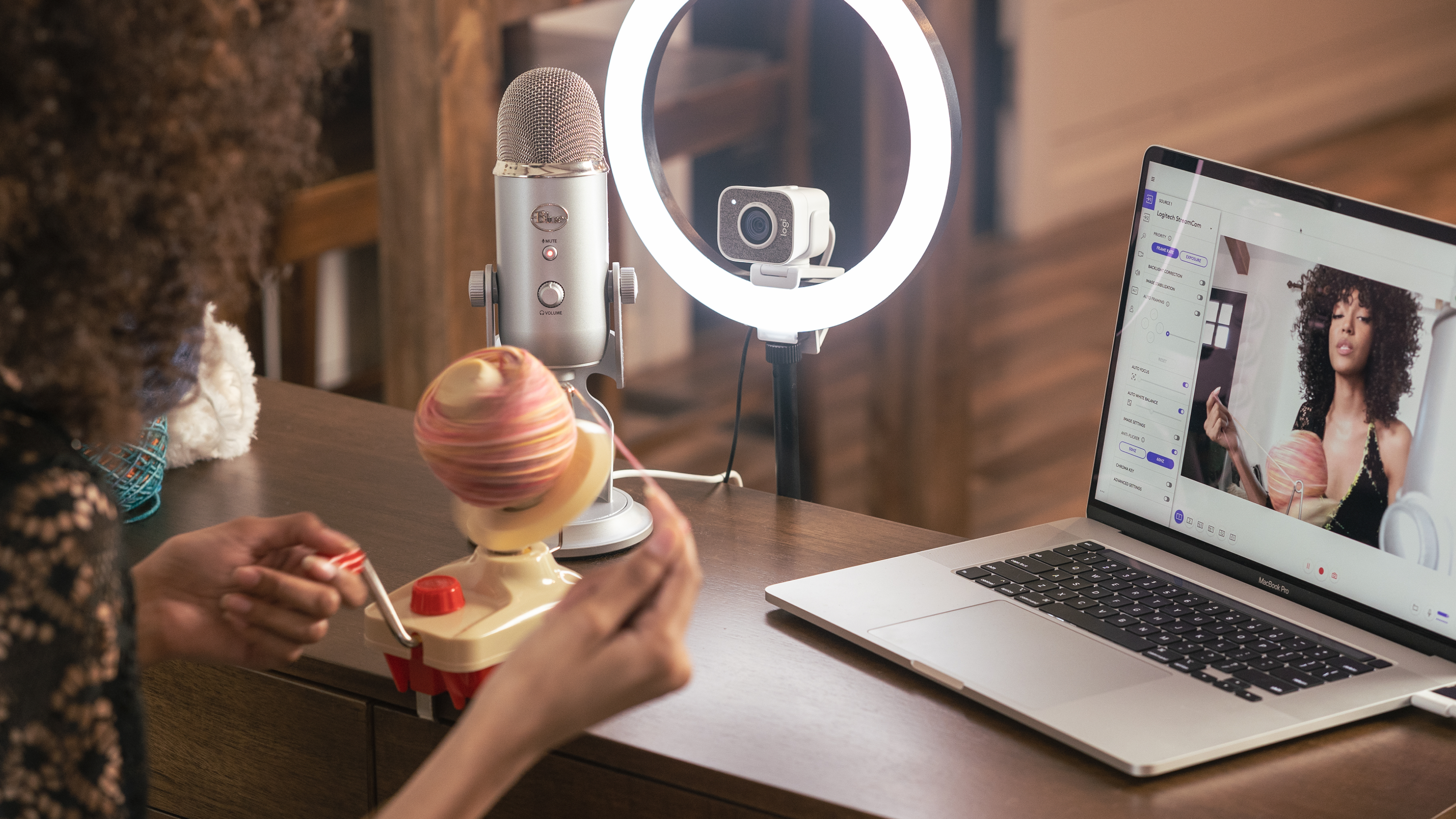 Osoba kręci nawijarką do włóczki, obok mikrofonu, kamery i laptopa.