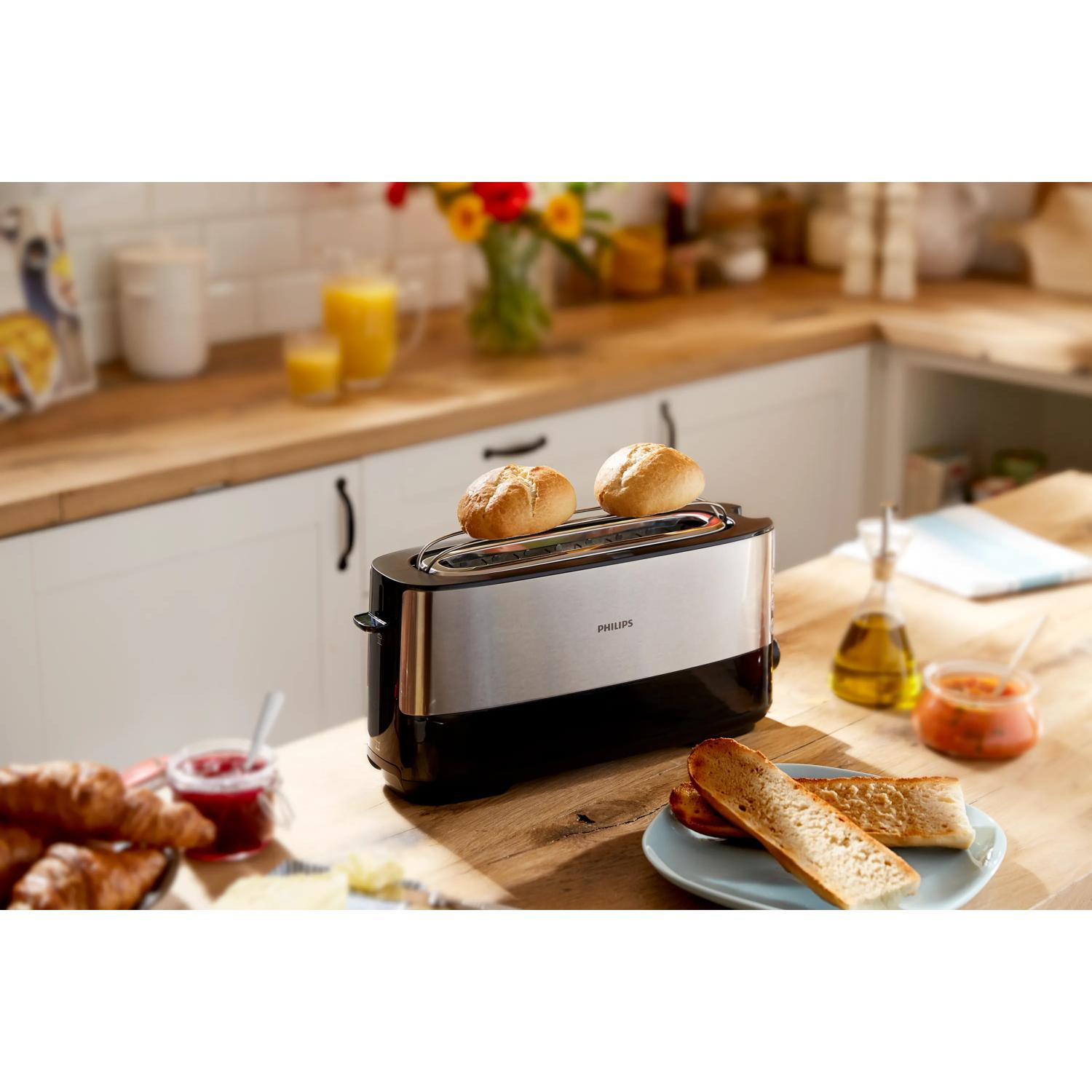 Ein Toaster mit zwei Brötchen, daneben Croissants, Marmelade, Brot und Sauce.