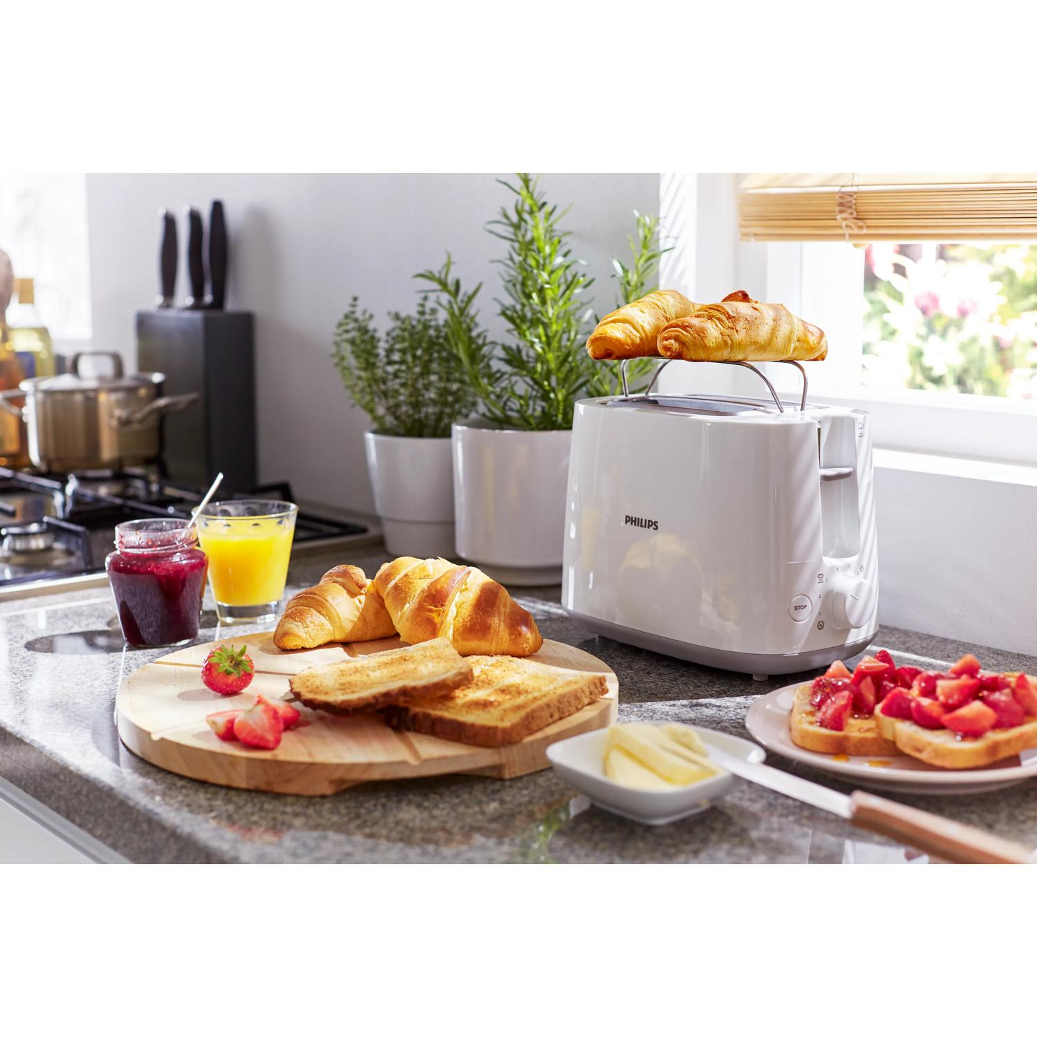 Un tostapane bianco con due croissant sopra, accanto a toast, marmellata e succo.