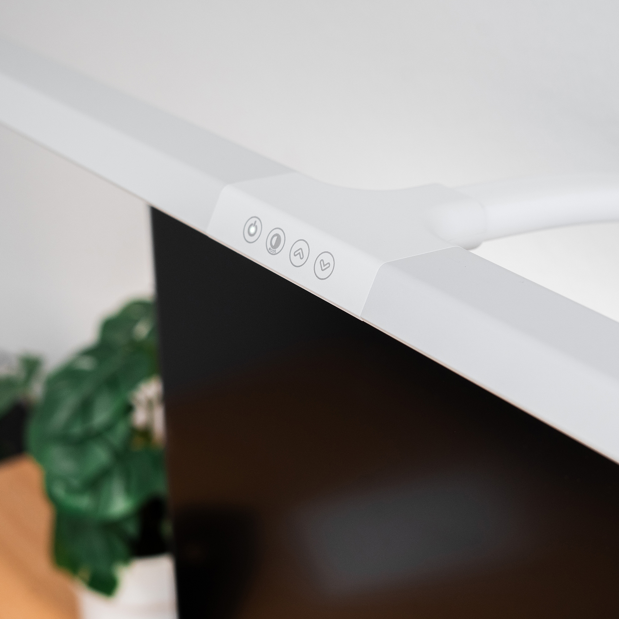 Un braccio di lampada da scrivania bianco con pulsanti di controllo sopra uno schermo scuro.