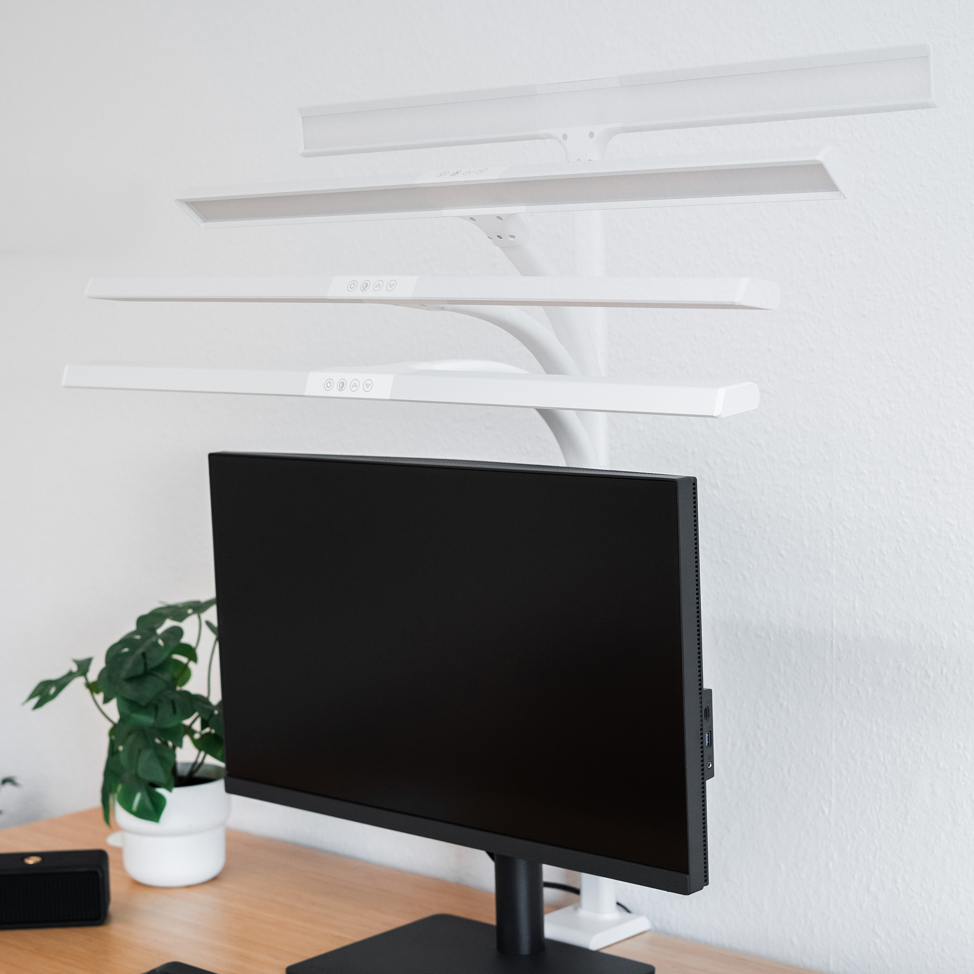 Una scrivania con monitor, lampada e pianta. La lampada è montata sopra il monitor.