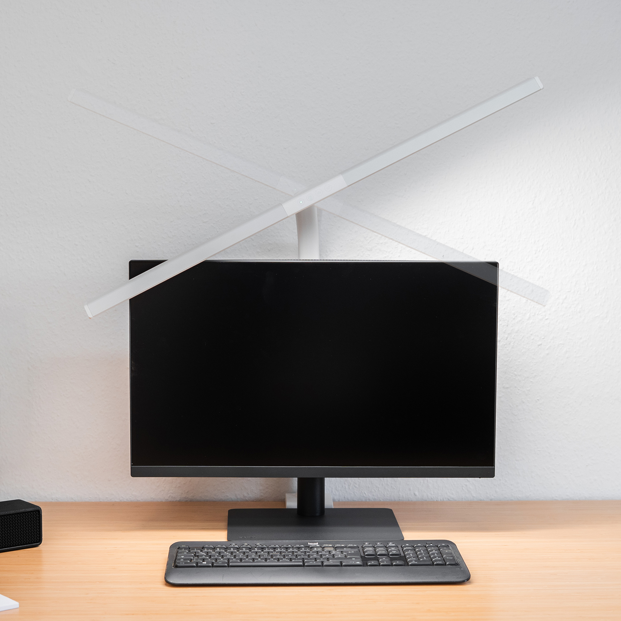 Un monitor nero si trova su una scrivania di legno con una tastiera davanti.