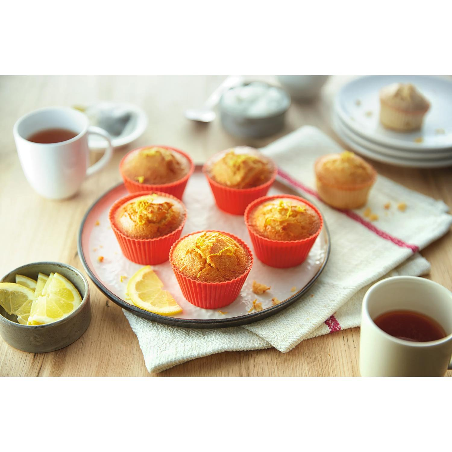Kırmızı kalıplarda altı muffin, limon kabuğu rendesiyle, çay ve limon dilimleri.