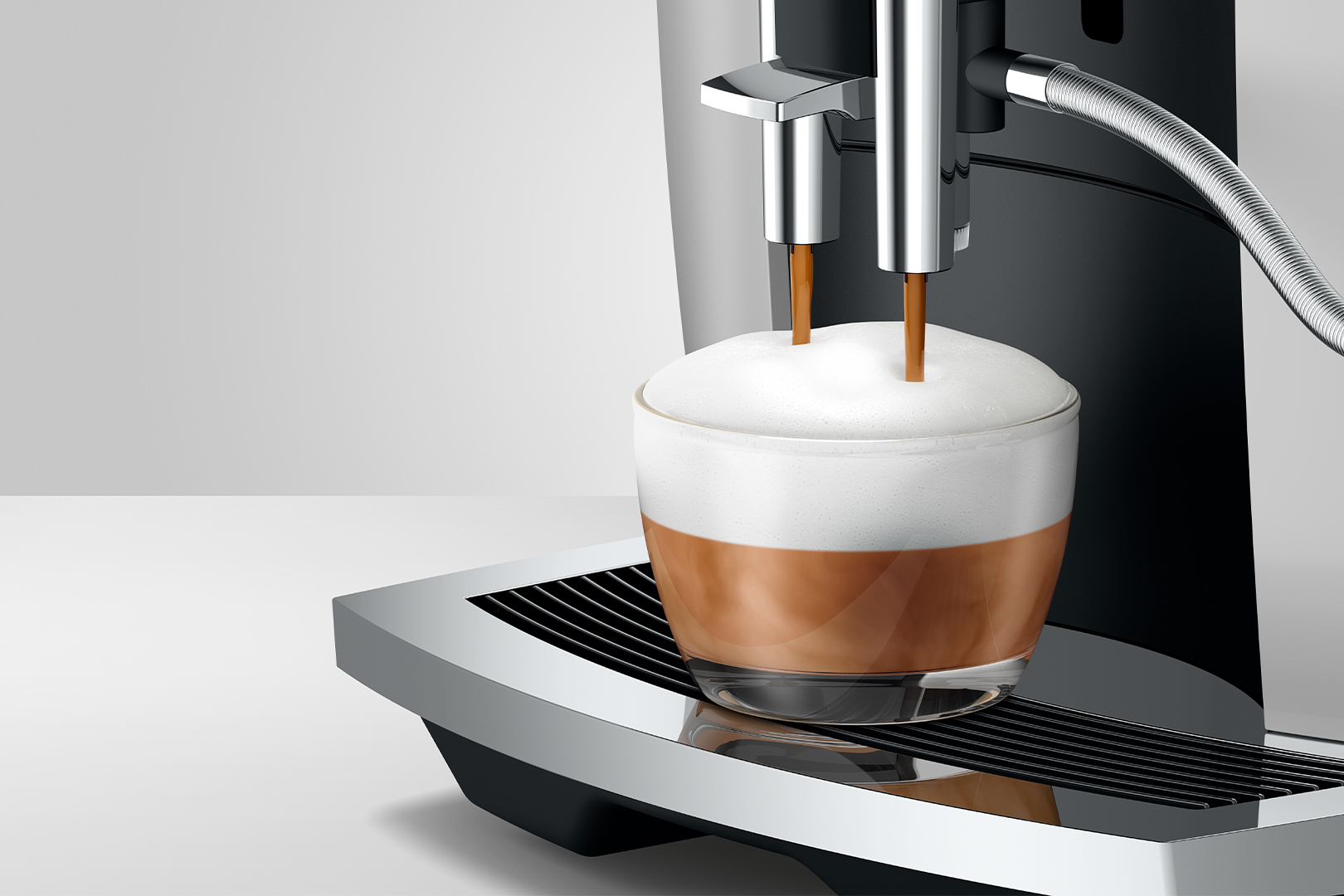 Ekspres do kawy parzy latte macchiato do szklanki z dużą ilością pianki mlecznej.