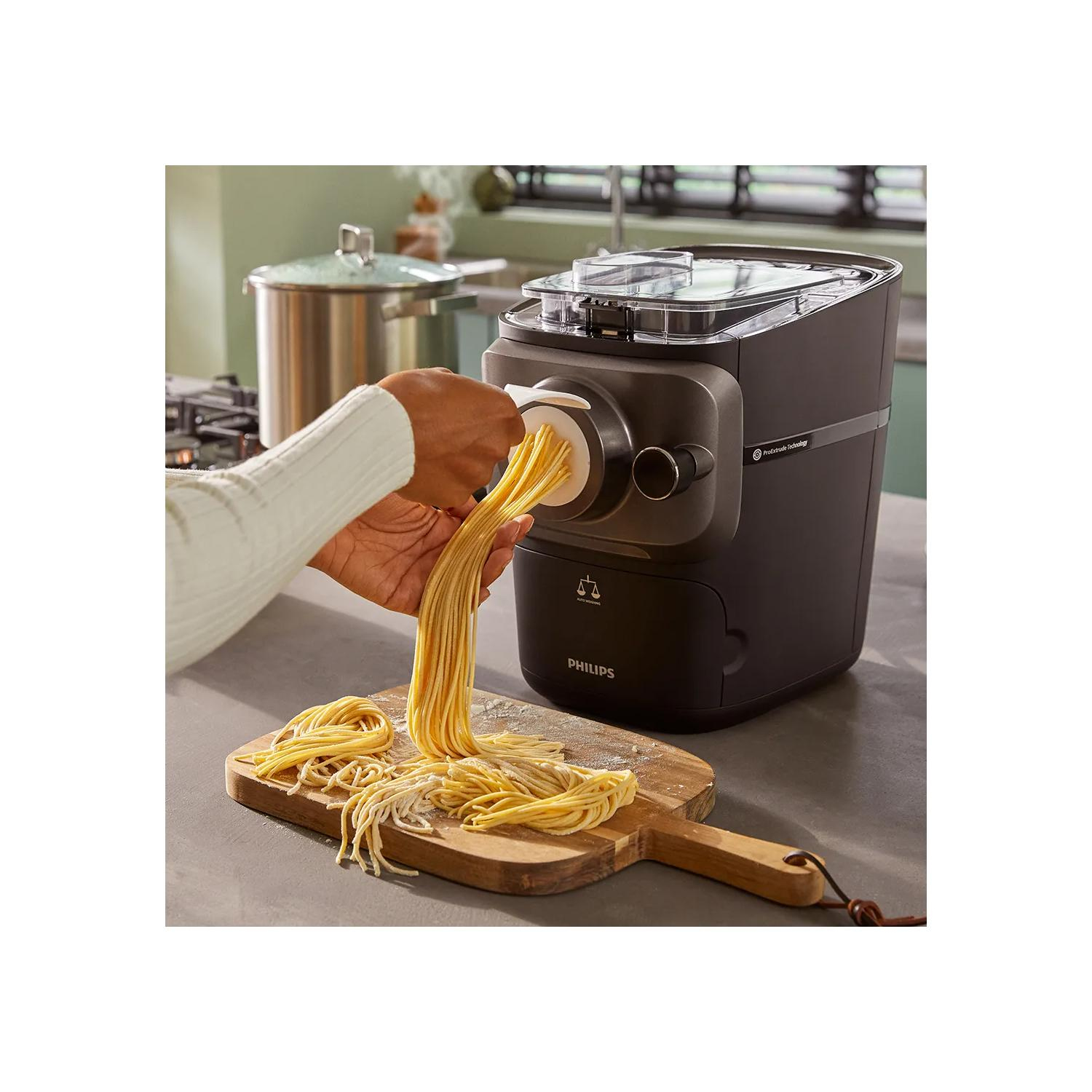 Eine Person benutzt eine Nudelmaschine, um frische Pasta herzustellen. Die Pasta liegt auf einem Holzbrett.