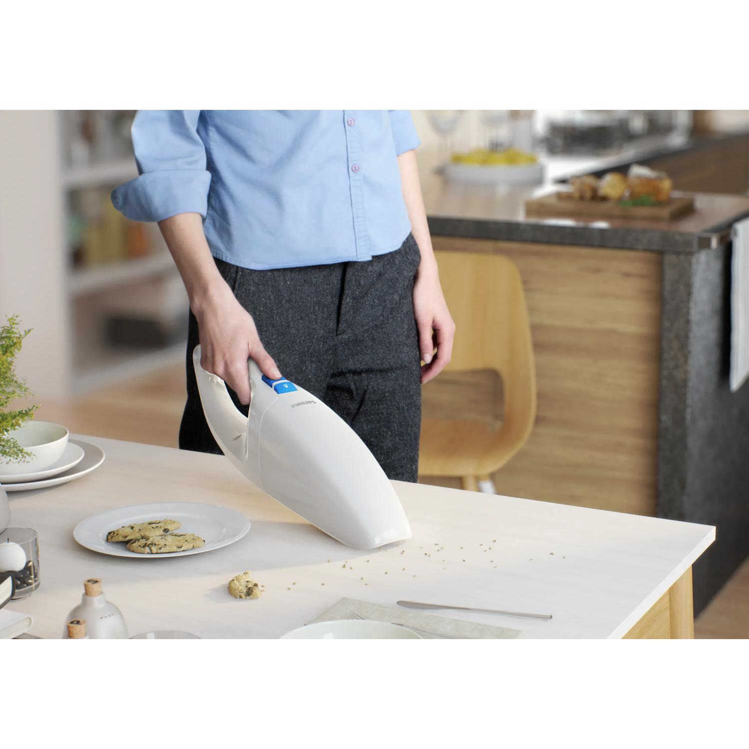 A person uses a white handheld vacuum to clean crumbs from a table.