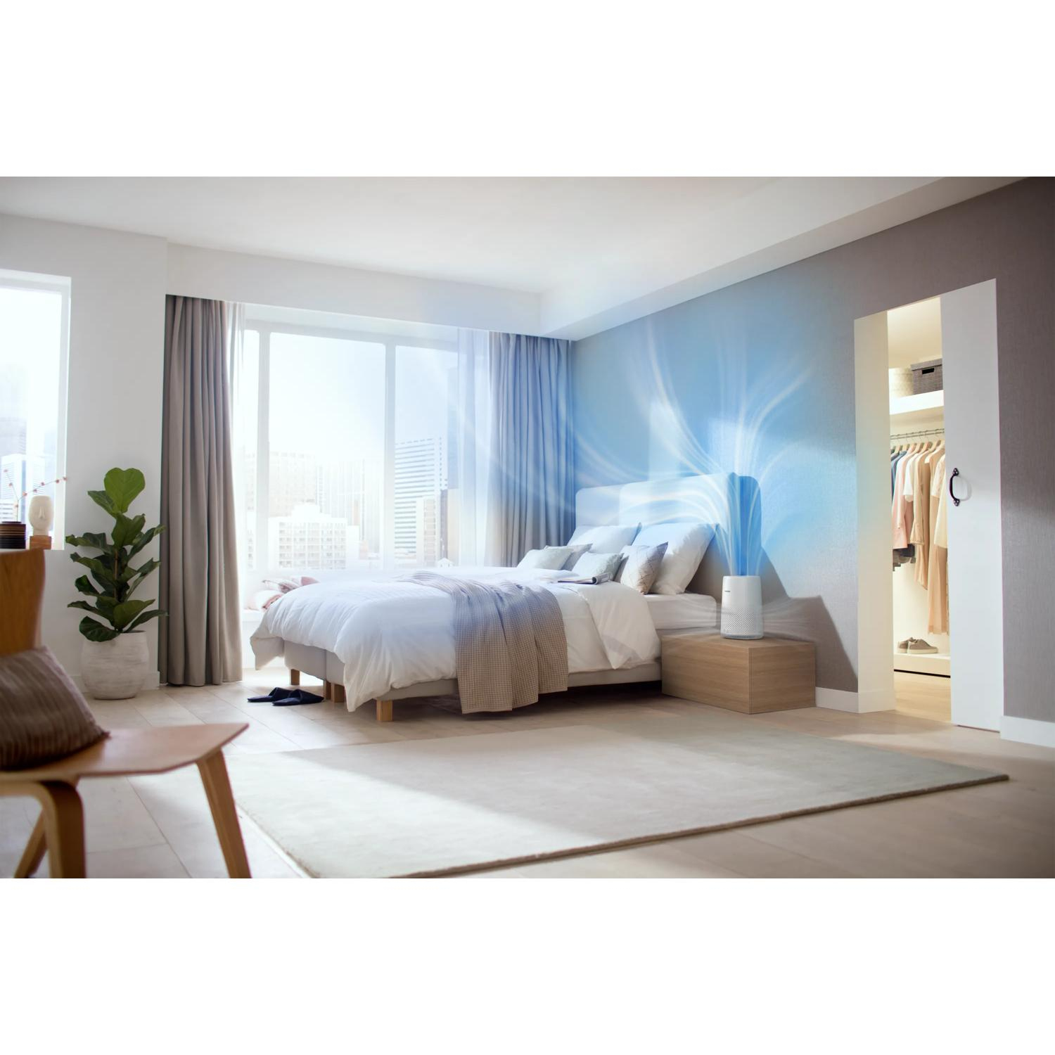 Un purificatore d'aria bianco su un comodino in una camera da letto con letto e finestra.