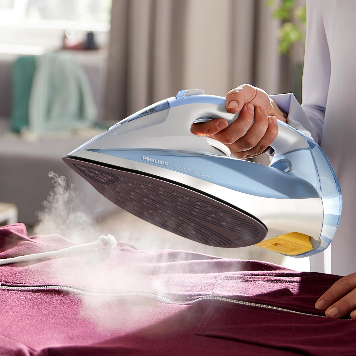 A Philips iron steams a maroon garment. A hand holds the iron.