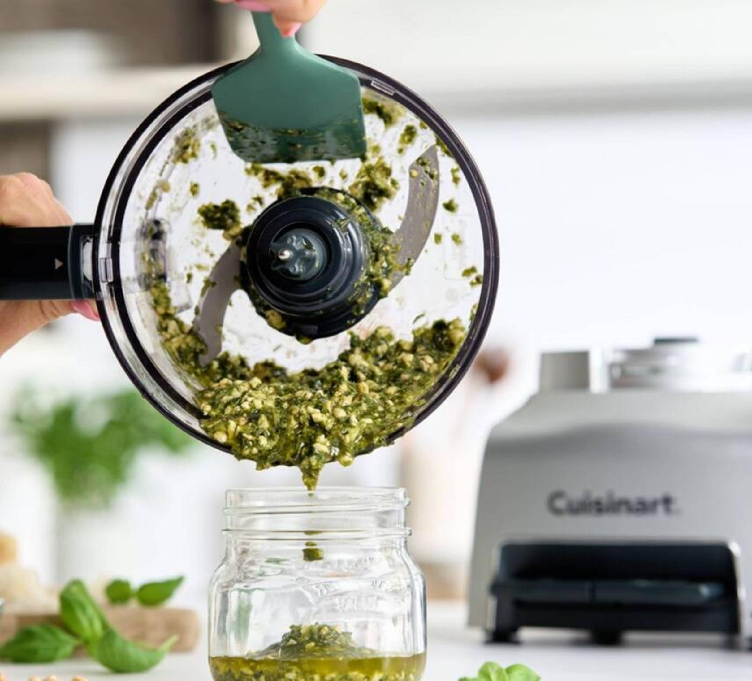 Il pesto verde viene raschiato da un robot da cucina in un barattolo con una spatola.