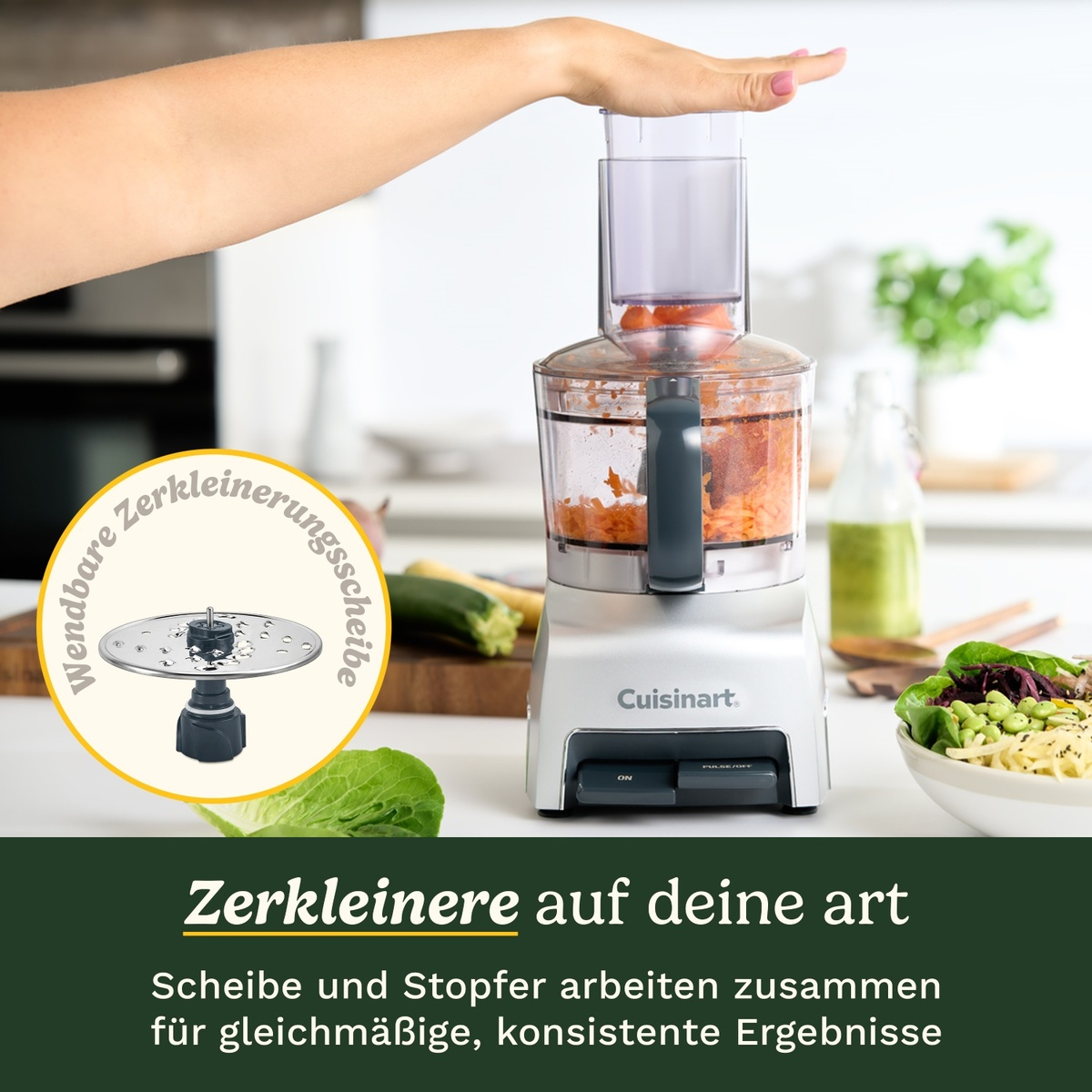 Un robot da cucina Cuisinart trita carote. Una mano tiene lo spingitore.