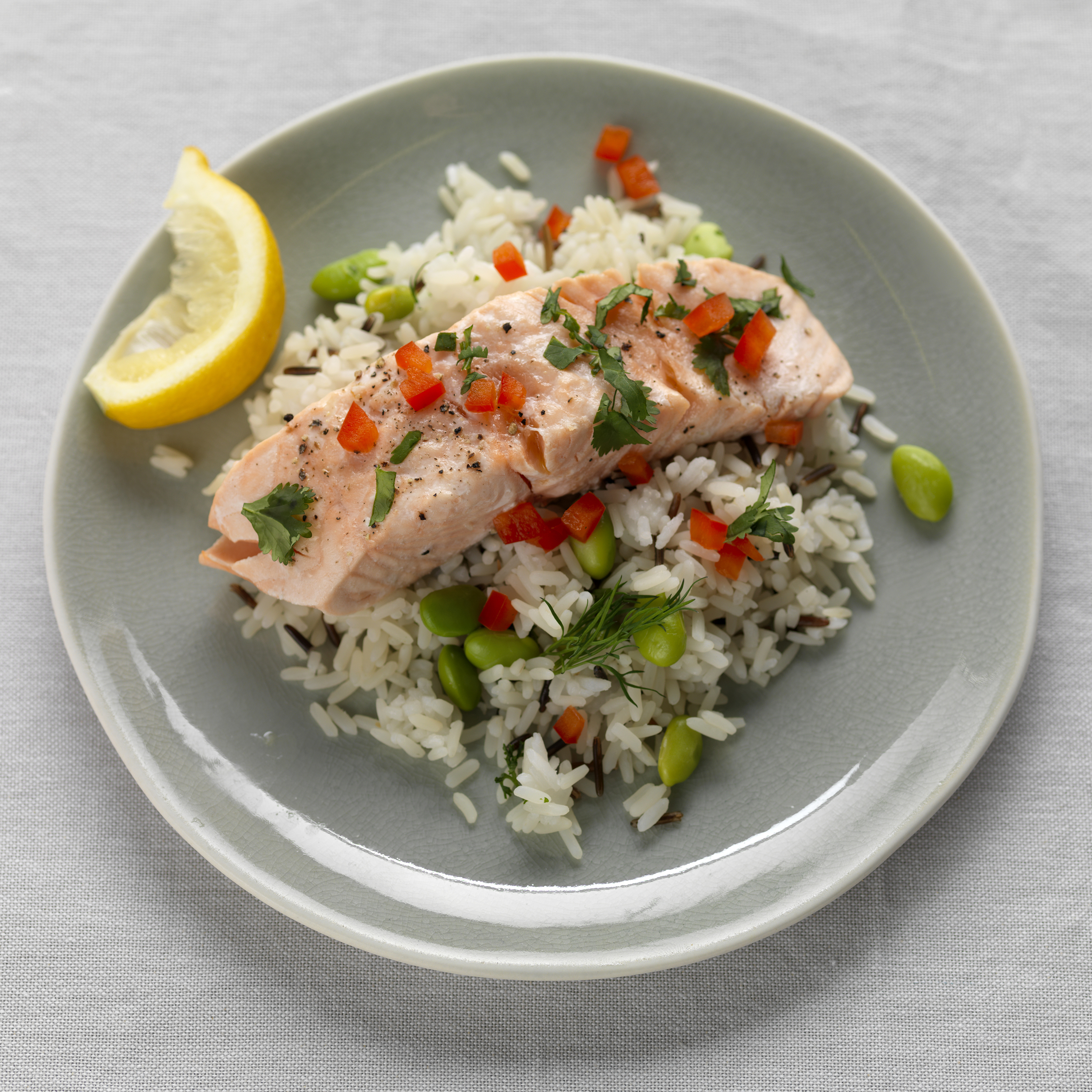 Lachsfilet auf Reis mit Erbsen, Paprika und Zitrone auf einem grauen Teller.