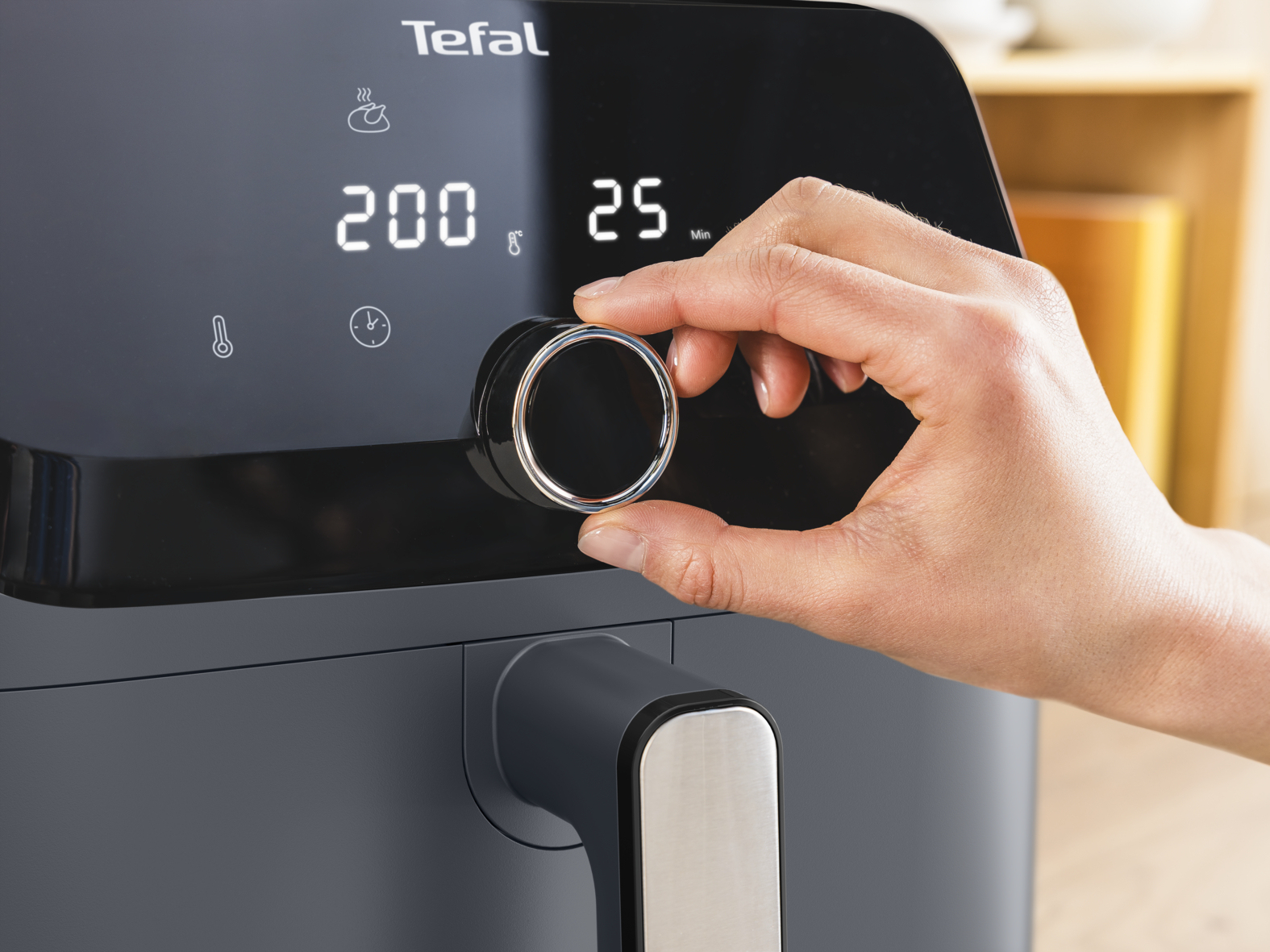 Eine Hand stellt einen Knopf an einem Tefal Heißluftfritteusen-Display ein, das 200 Grad und 25 Minuten anzeigt.