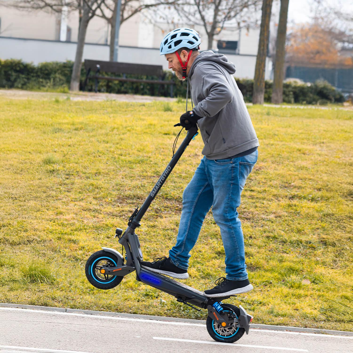 Un hombre monta un patinete eléctrico por un camino, con una rueda en el aire.