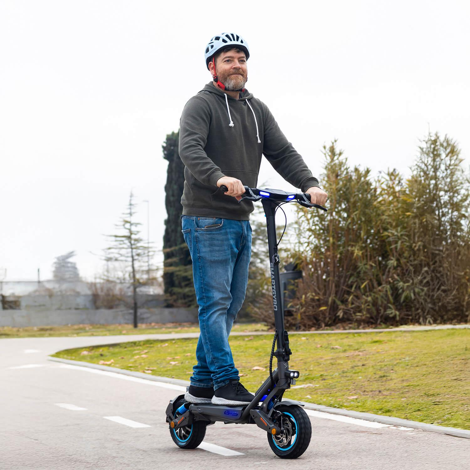 Un hombre con barba monta un patinete eléctrico negro en un carril bici.