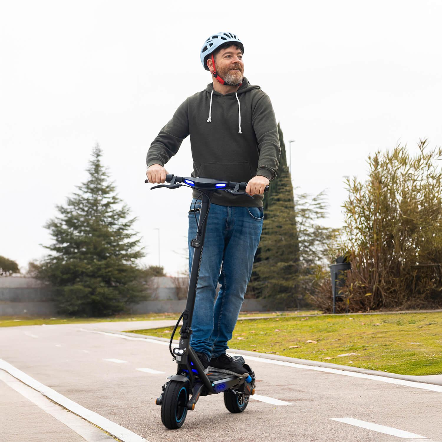 Hombre monta patinete eléctrico en carril bici, con casco y sudadera.