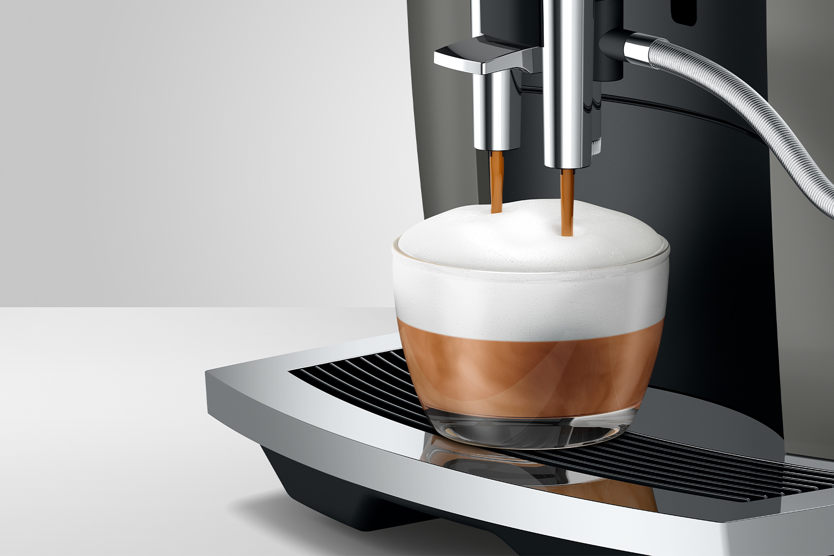 Eine Kaffeemaschine brüht einen Latte Macchiato in ein Glas mit viel Milchschaum.