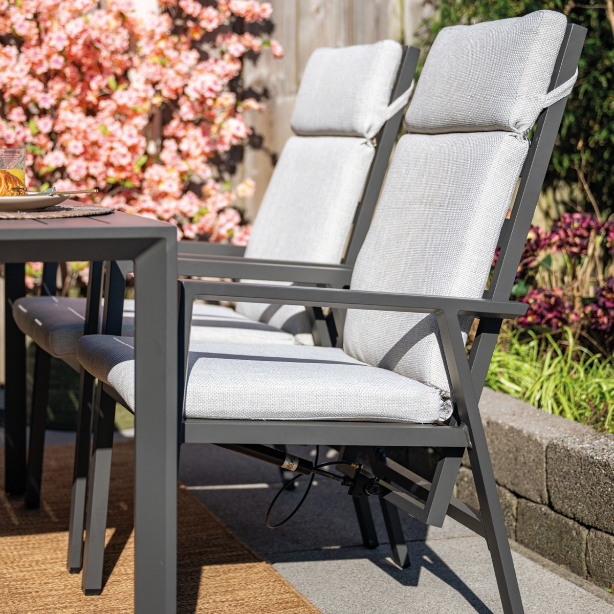 Twee grijze tuinstoelen met beige kussens staan naast een tafel in de tuin.