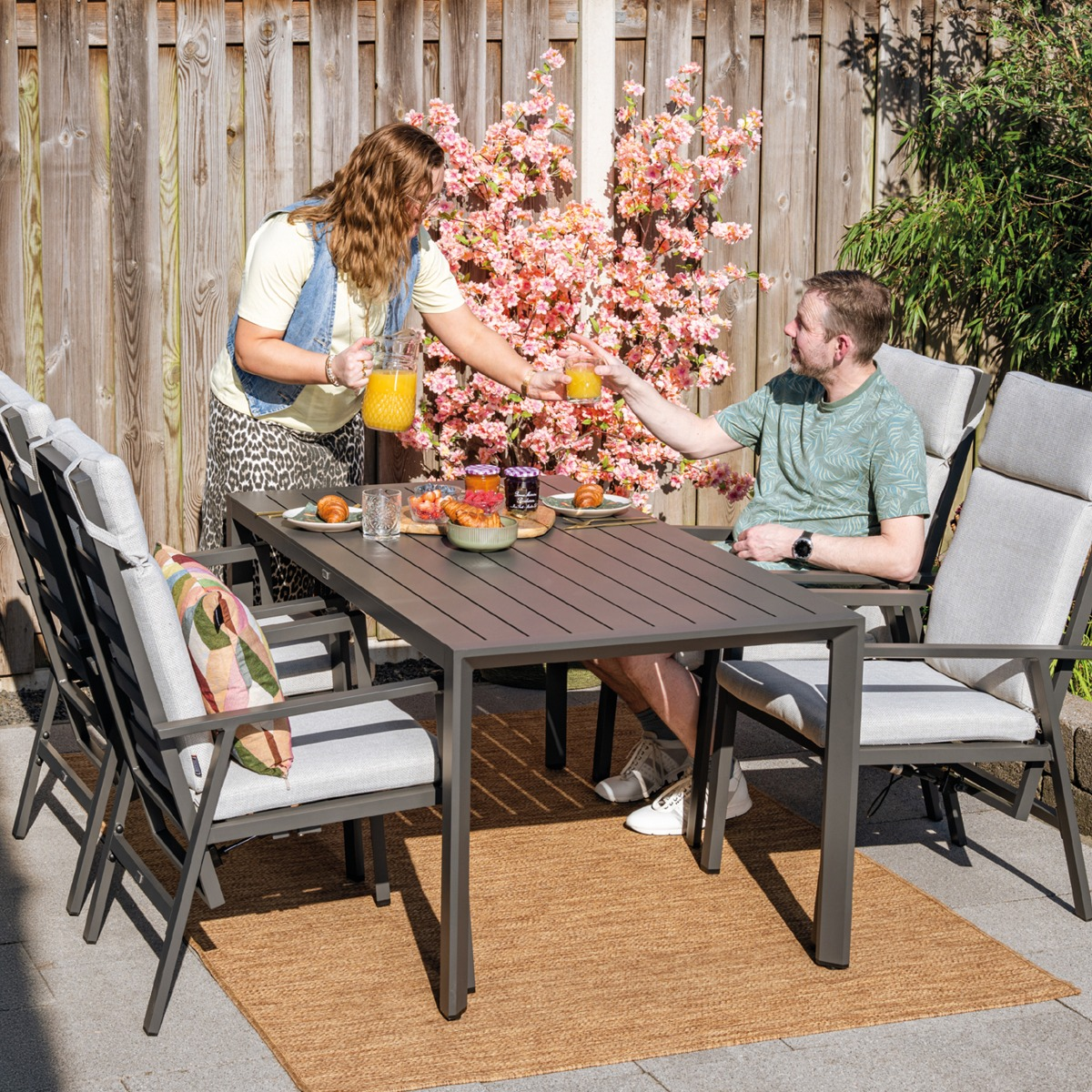 Man en vrouw serveren ontbijt in tuin naast bloeiende boom.