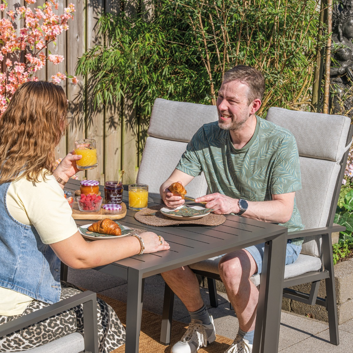 Een stel ontbijt buiten aan tafel met croissants, jam en sap.