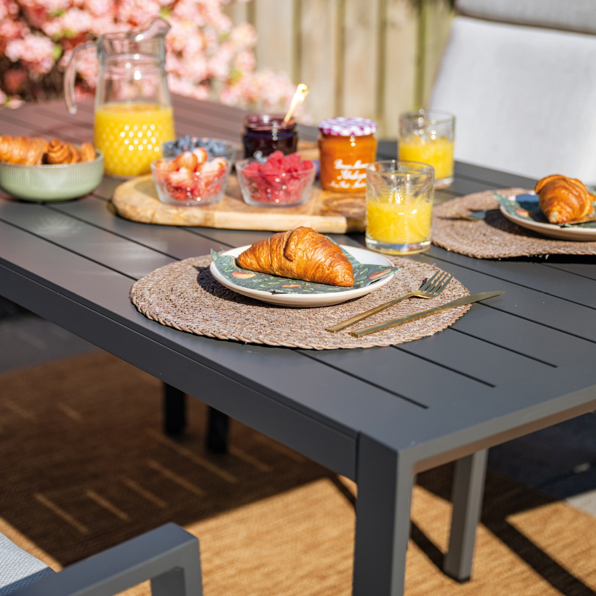 Een ontbijttafel gedekt met croissants, fruit, jam en sinaasappelsap.