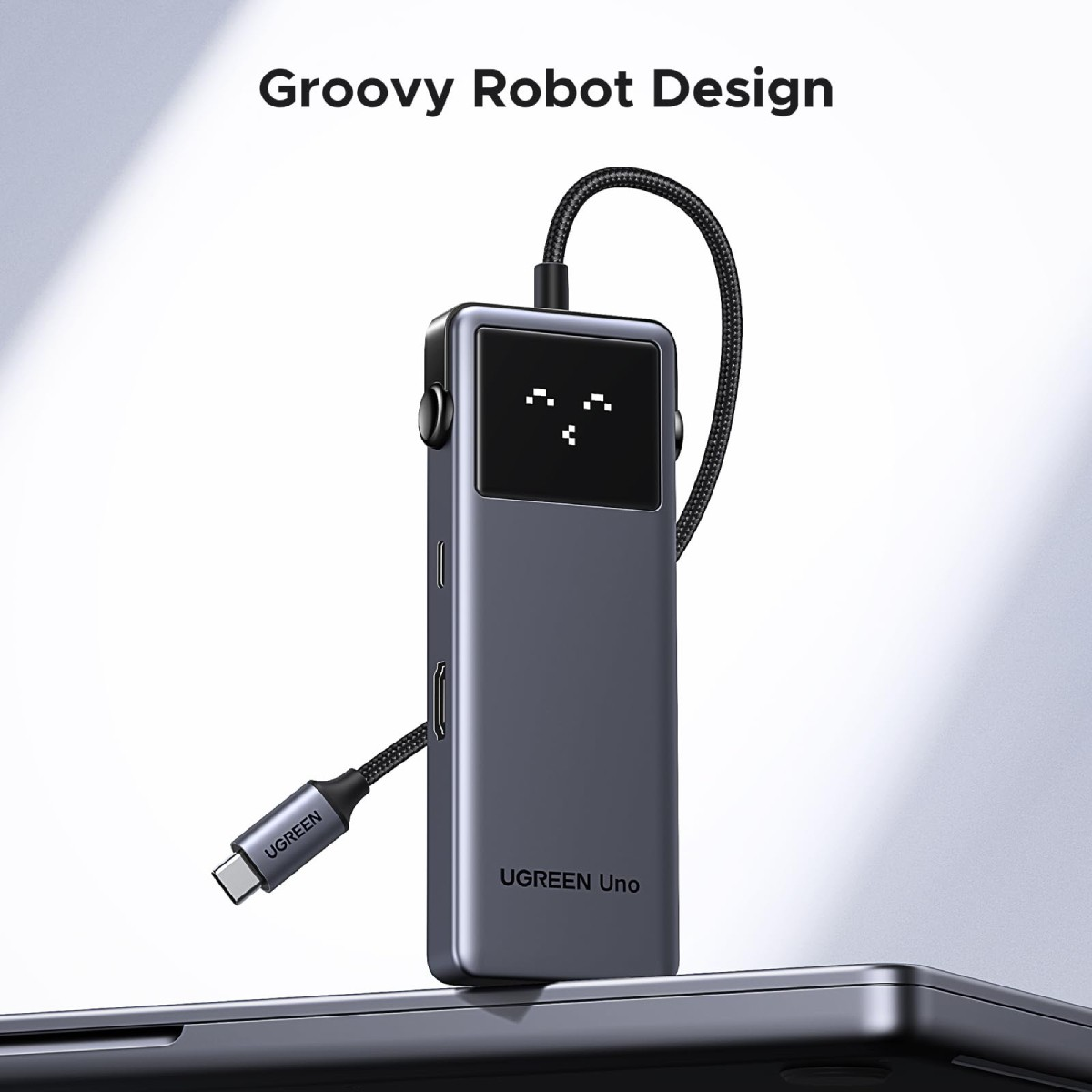 Szary hub USB-C UGREEN Uno z ekranem wyświetlającym twarz robota, na powierzchni.