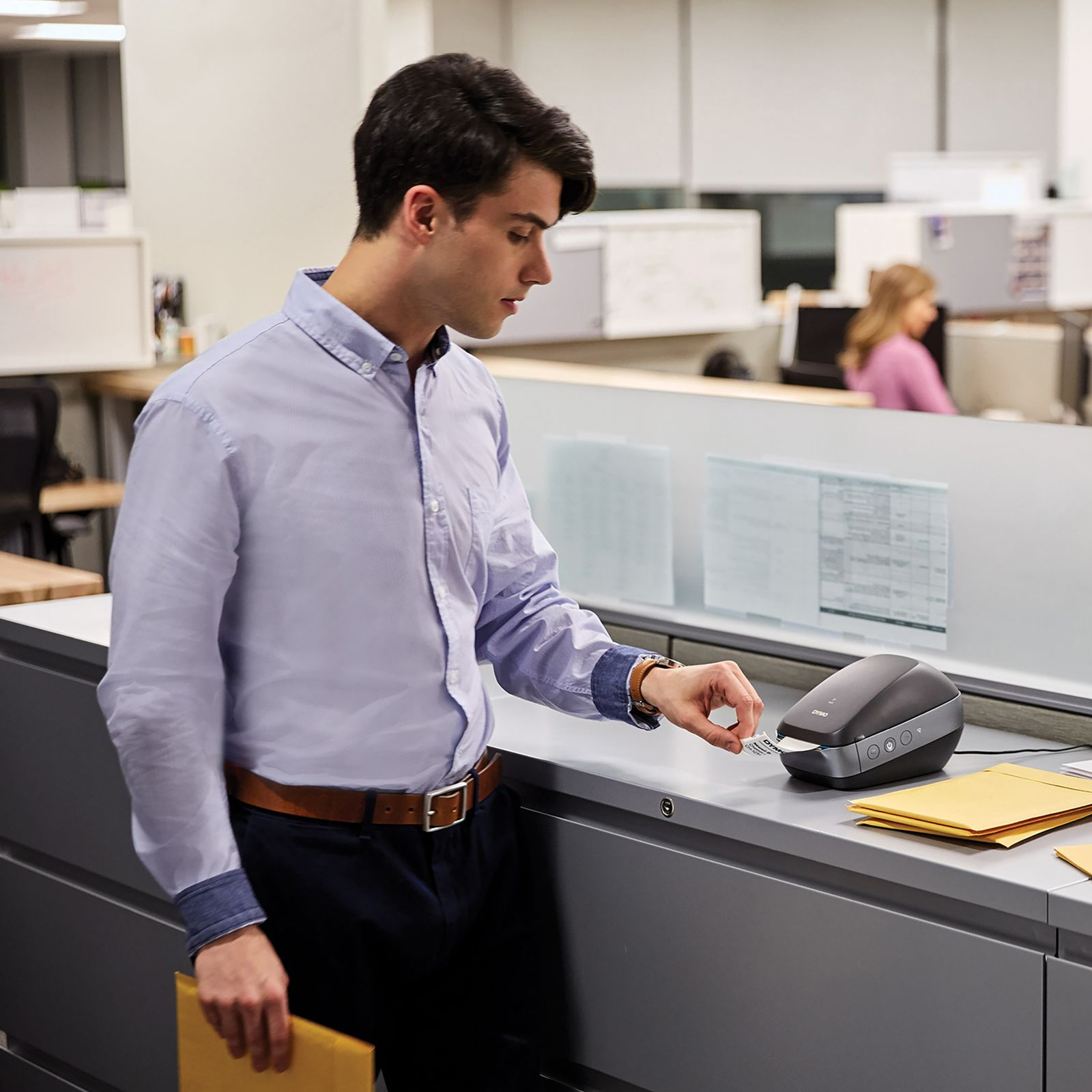 Man printing a label. Man in blue shirt with brown belt and label printer.