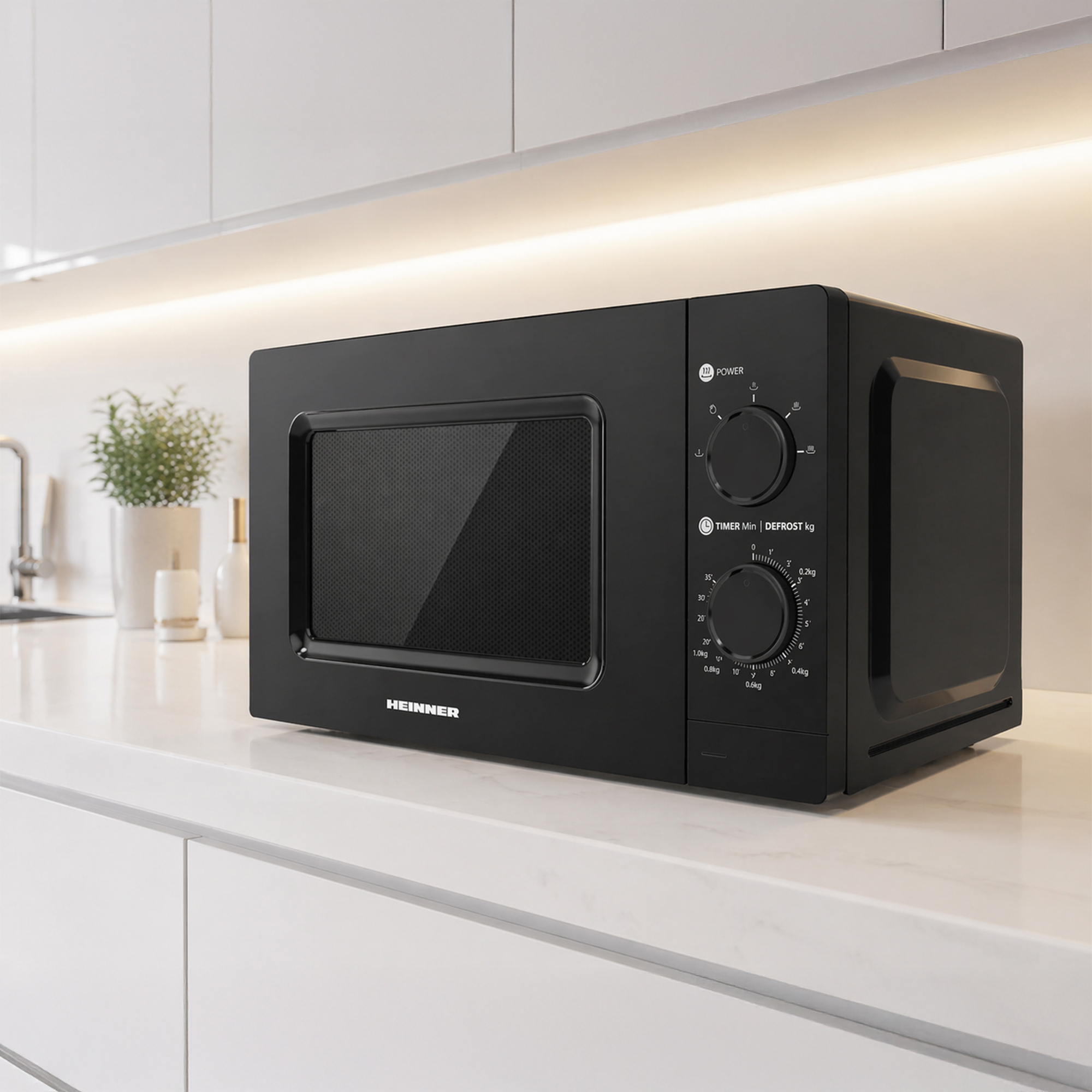 A black Heinner microwave sits on a white countertop with cabinets above and a plant to the left.