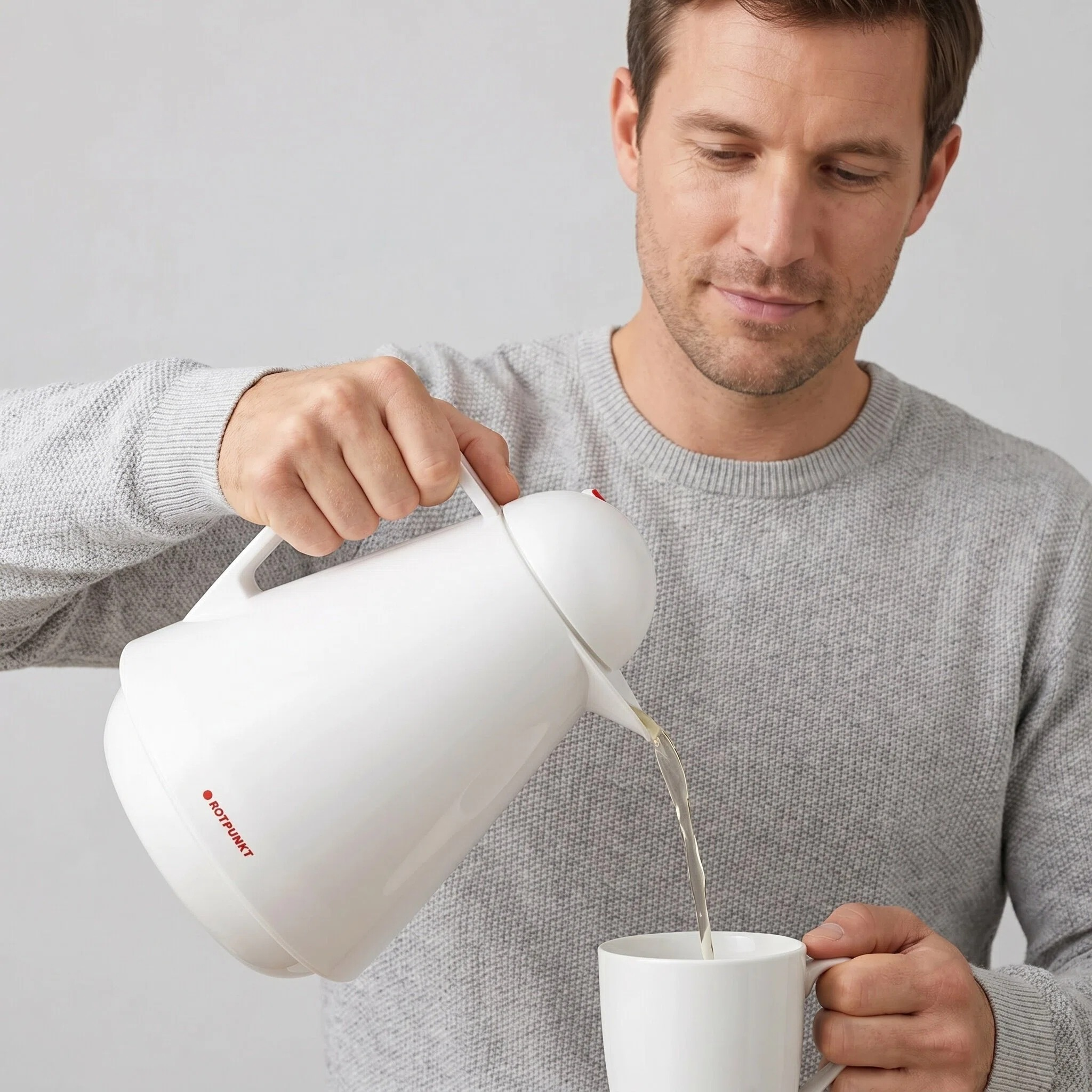 Ein Mann gießt Flüssigkeit aus einer weißen Thermoskanne in eine weiße Tasse.