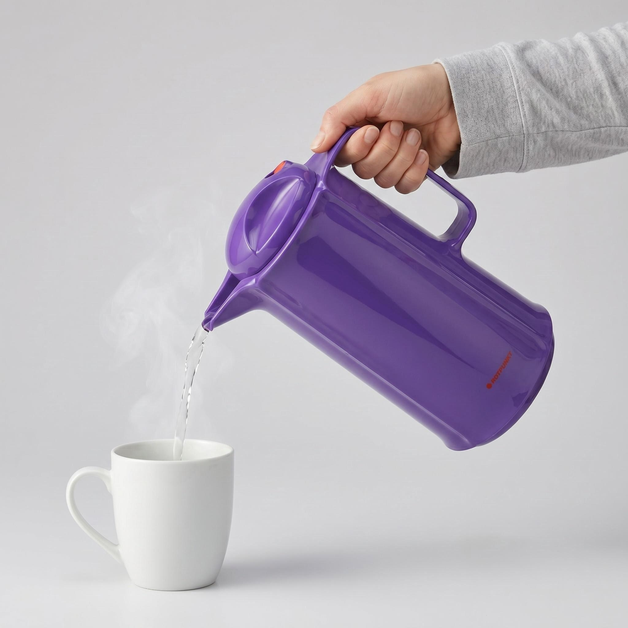 Eine Hand gießt dampfendes Wasser aus einer lila Kanne in eine weiße Tasse.