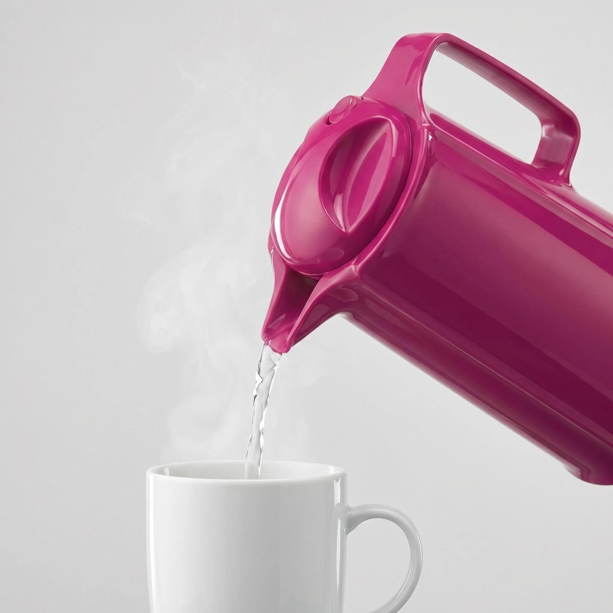 Eine pinkfarbene Kanne gießt heißes Wasser in eine weiße Tasse.