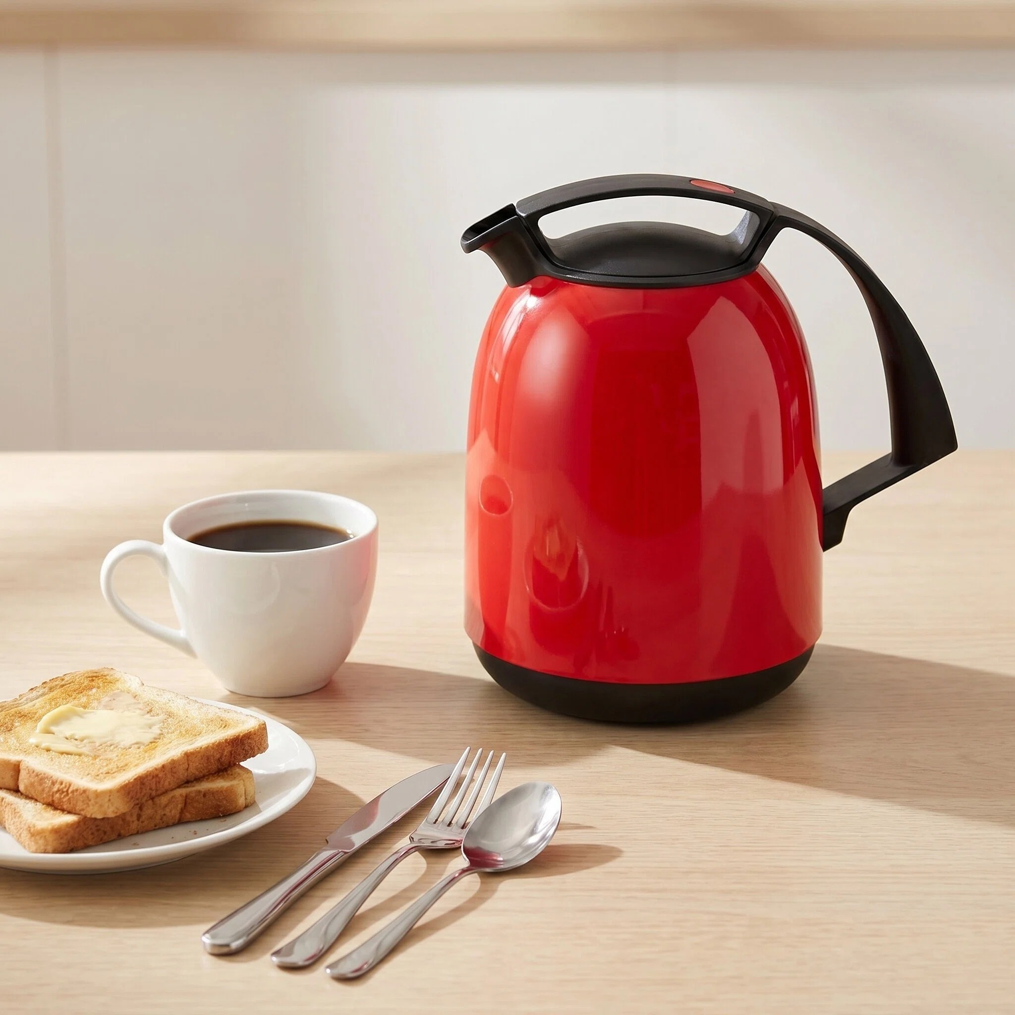 Roter Wasserkocher mit schwarzem Griff, daneben eine Tasse Kaffee und Toast.