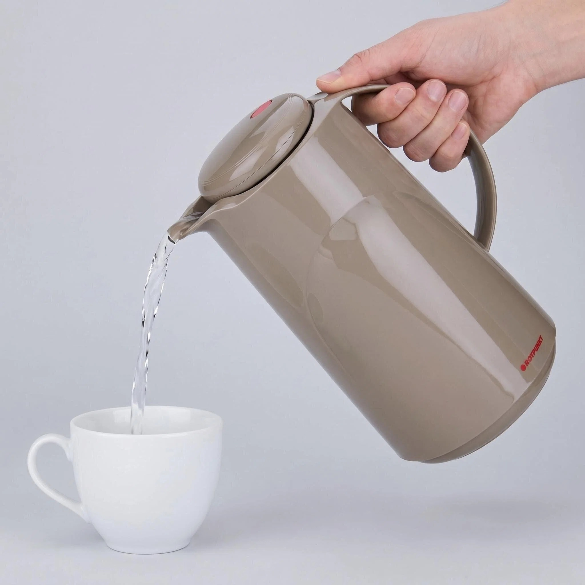 Una mano tiene un thermos beige, versa acqua in una tazza bianca.