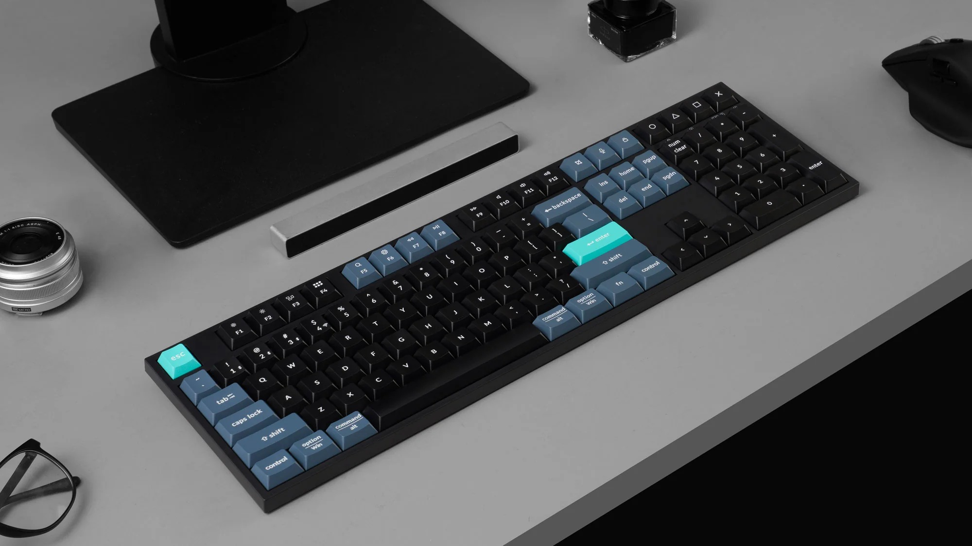 Czarna klawiatura mechaniczna z niebieskimi i turkusowymi klawiszami na szarym biurku.