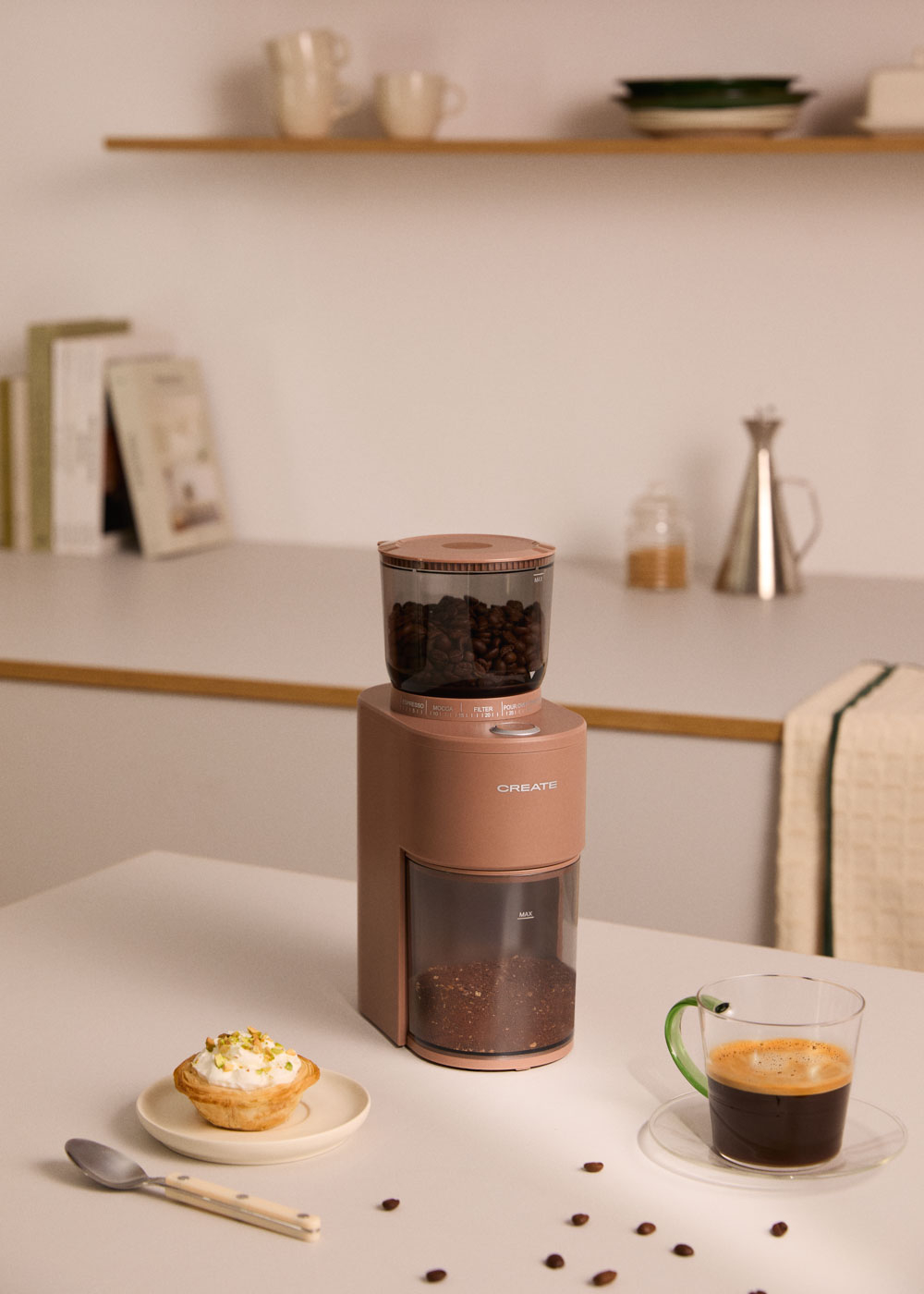 Un molinillo de café rosa con café y un pastel cerca.