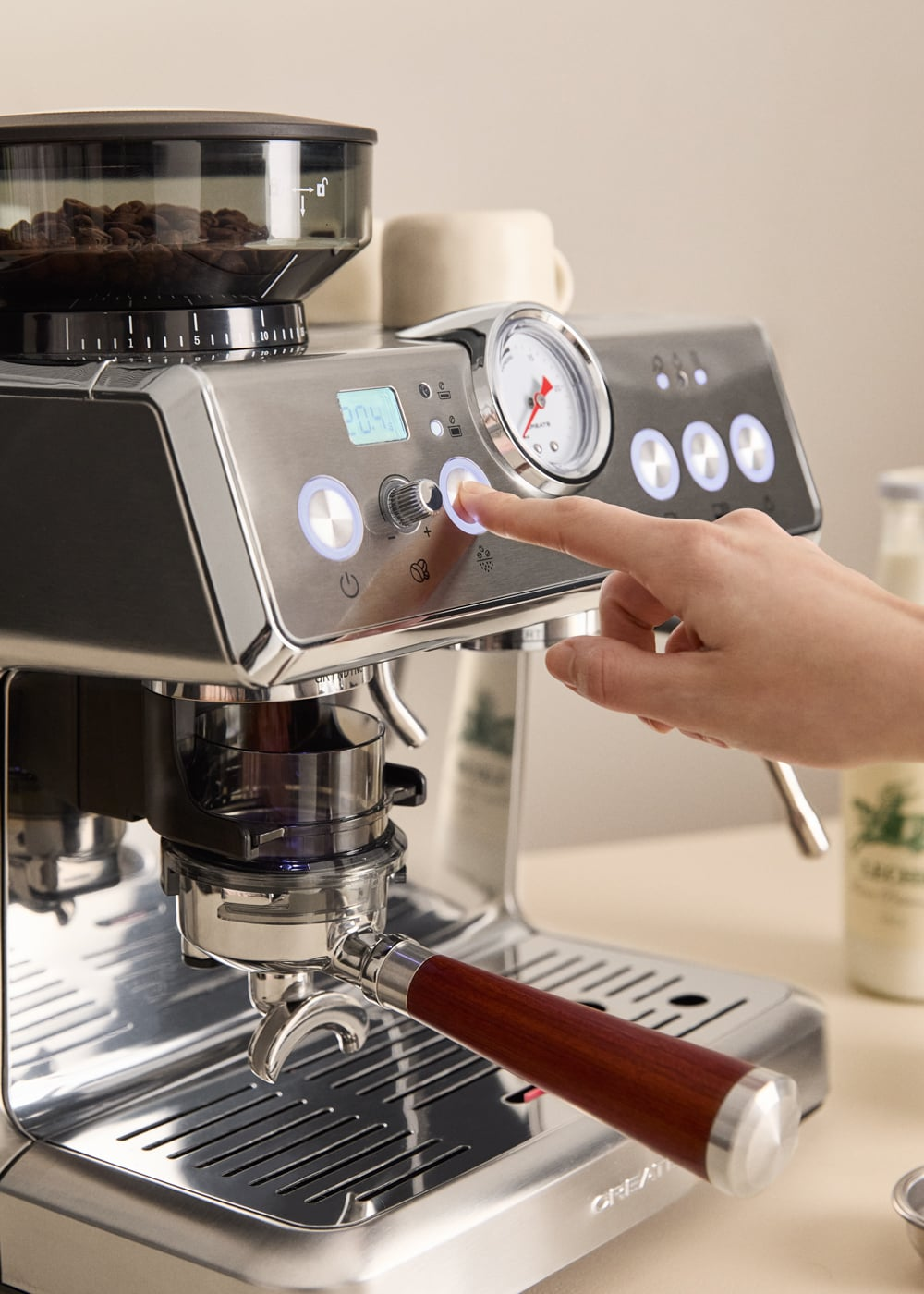Una mano presiona un botón en una máquina de espresso plateada con molinillo y manómetro.