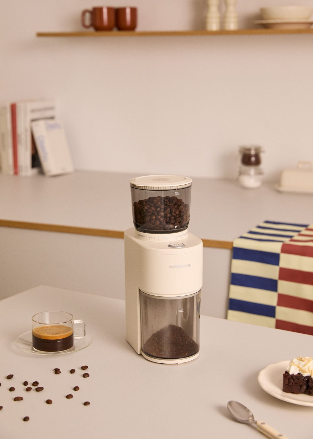 Un molinillo de café blanco con granos arriba y molido abajo, junto a una taza de espresso.