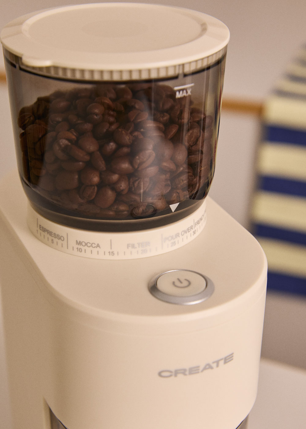 Primer plano de un molinillo de café color crema lleno de granos de café tostados.