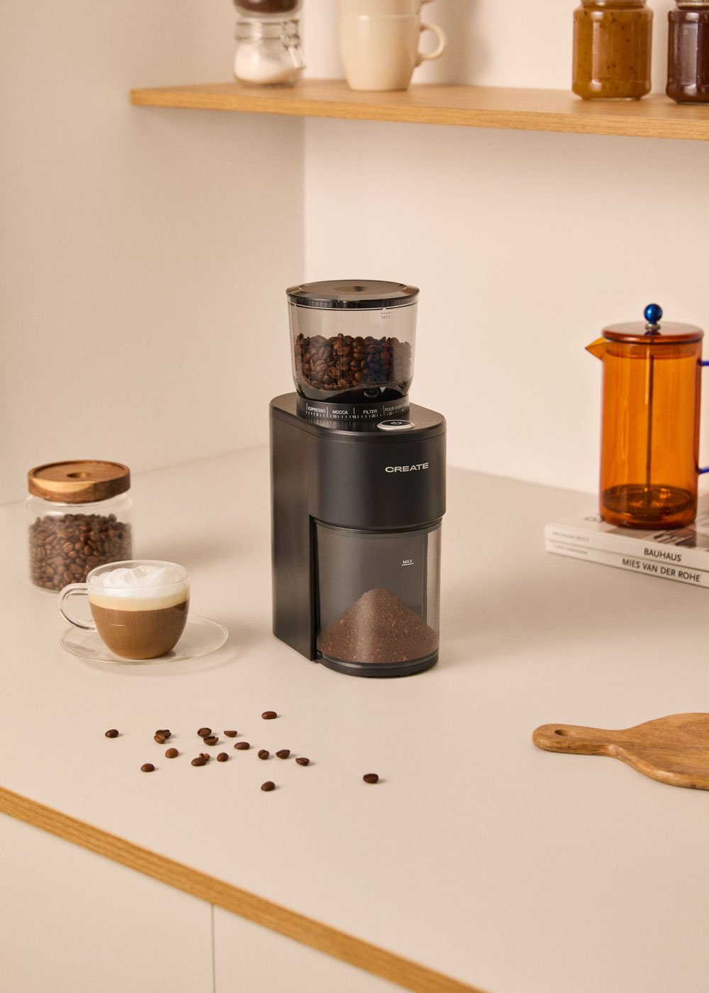 Un molinillo de café negro está en un mostrador con granos de café y una taza.