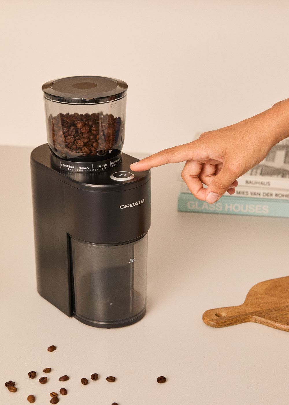 Un molinillo de café negro con granos; una mano presiona el botón.